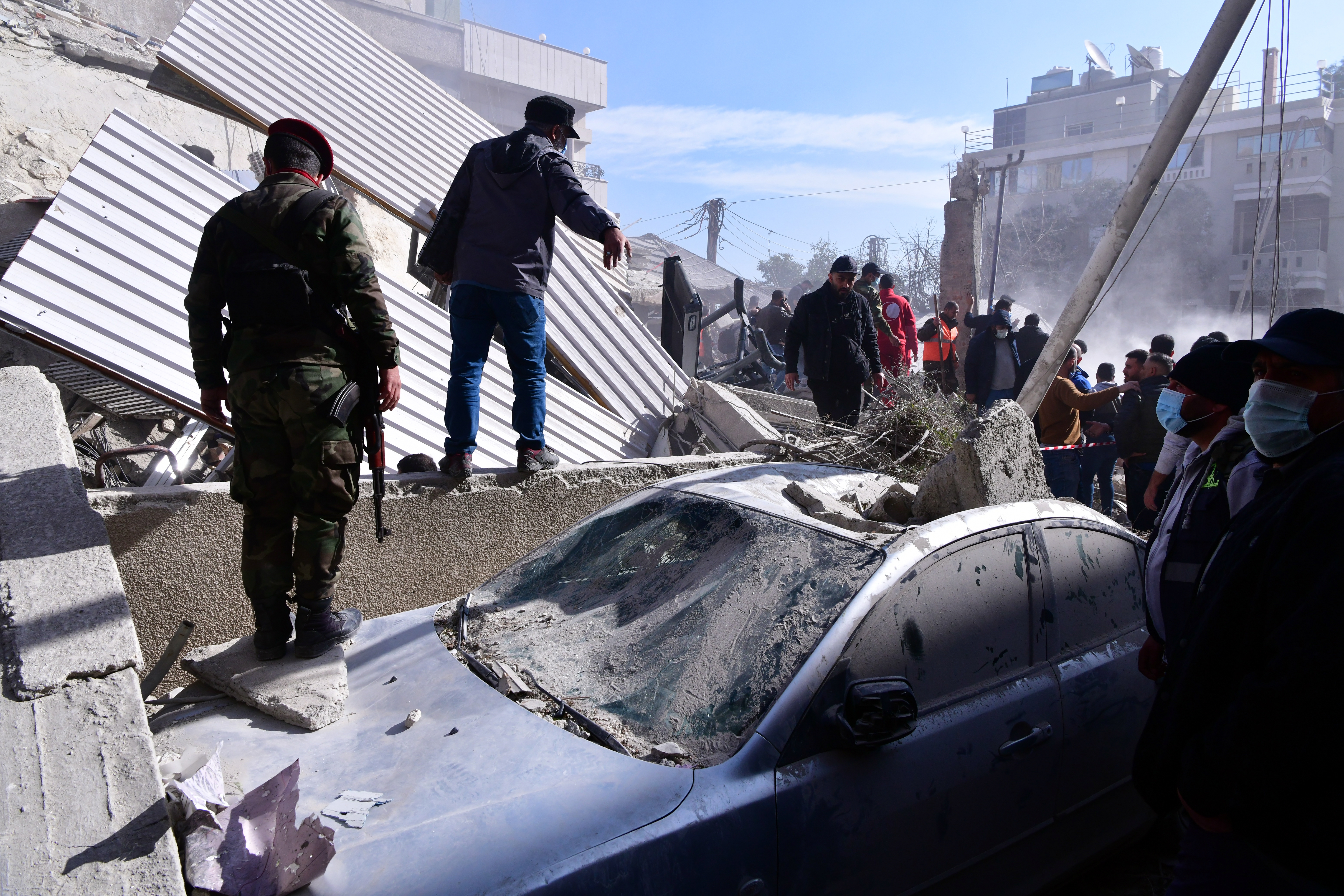 Soldiers and civilians check a damaged car at the site of a residential building that was hit in an alleged Israeli strike in Mazzeh neighborhood, Damascus, Syria, January 20, 2024
