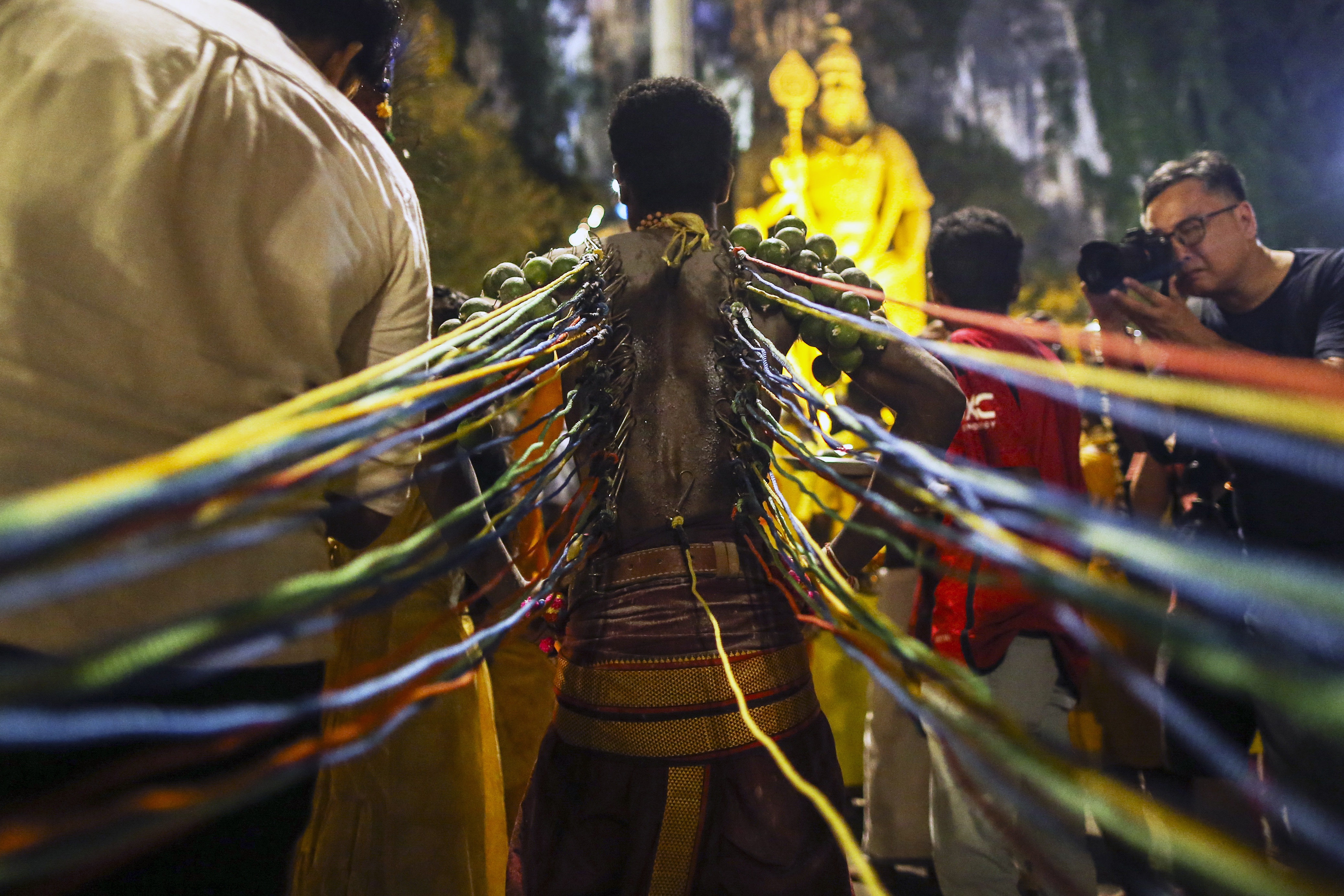 A man walking with hooks attached to his back. They are pulling his skin