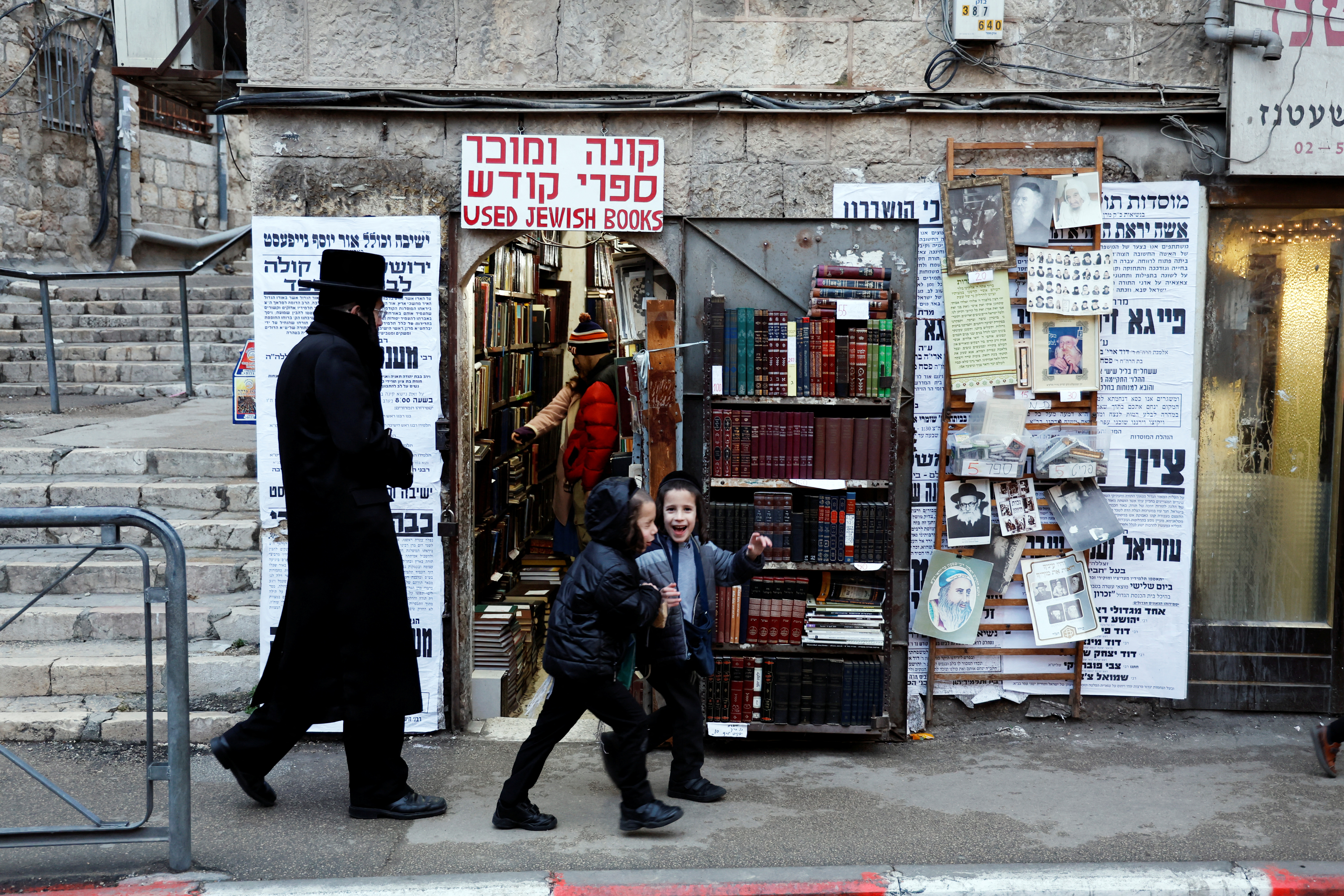 Ultra-Orthodox Jewish people walk past a shop which buys and sells used religious Jewish books on a commercial street in Jerusalem's Mea Shearim neighbourhood, January 2, 2023