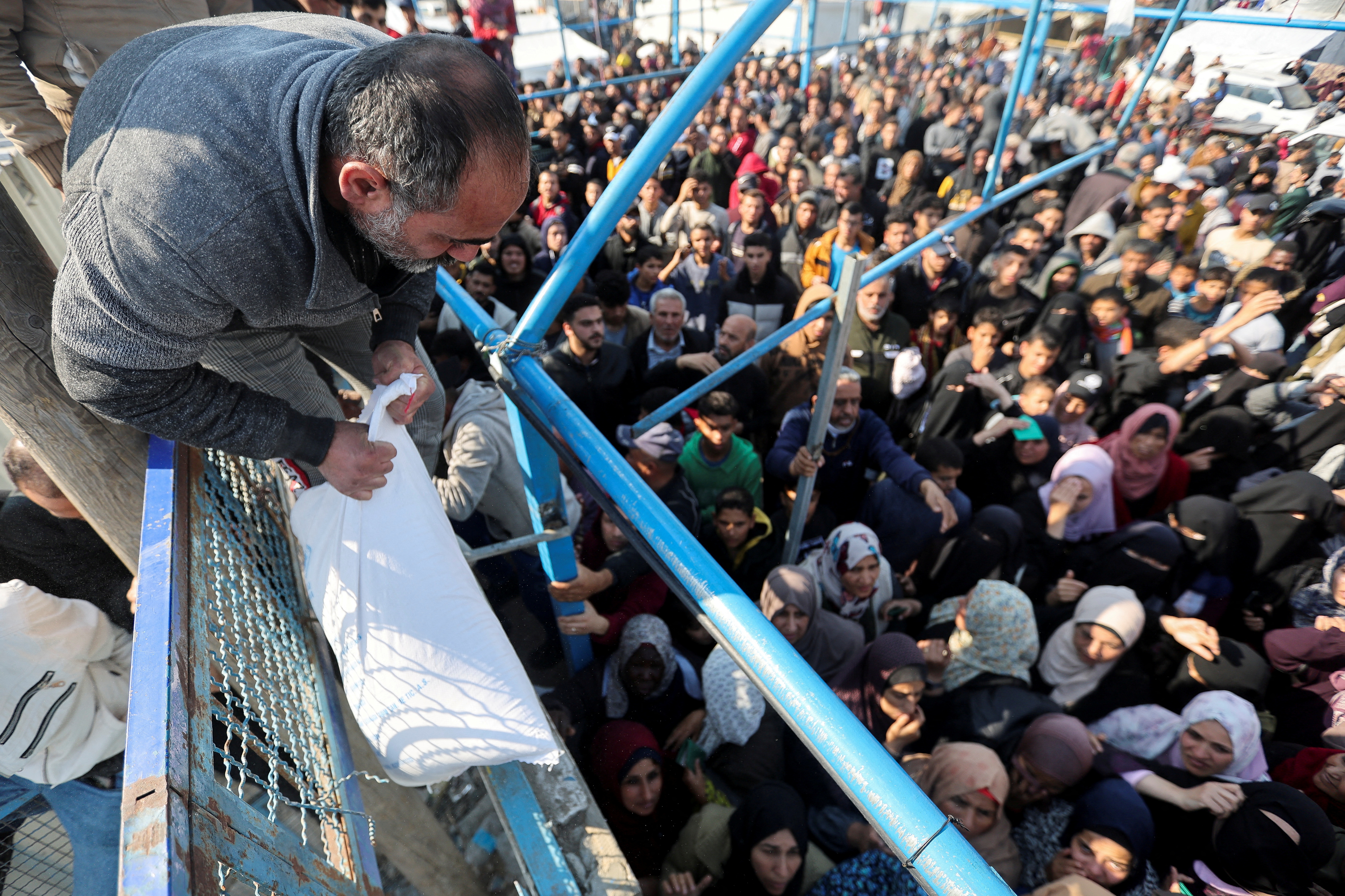 A Palestinian man holds a flour bag as others wait to receive theirs from the United Nations Relief and Works Agency (UNRWA) during a temporary truce between Hamas and Israel, in Khan Younis in the southern Gaza Strip, November 29, 2023. REUTERS/Ibraheem Abu Mustafa TPX IMAGES OF THE DAY
