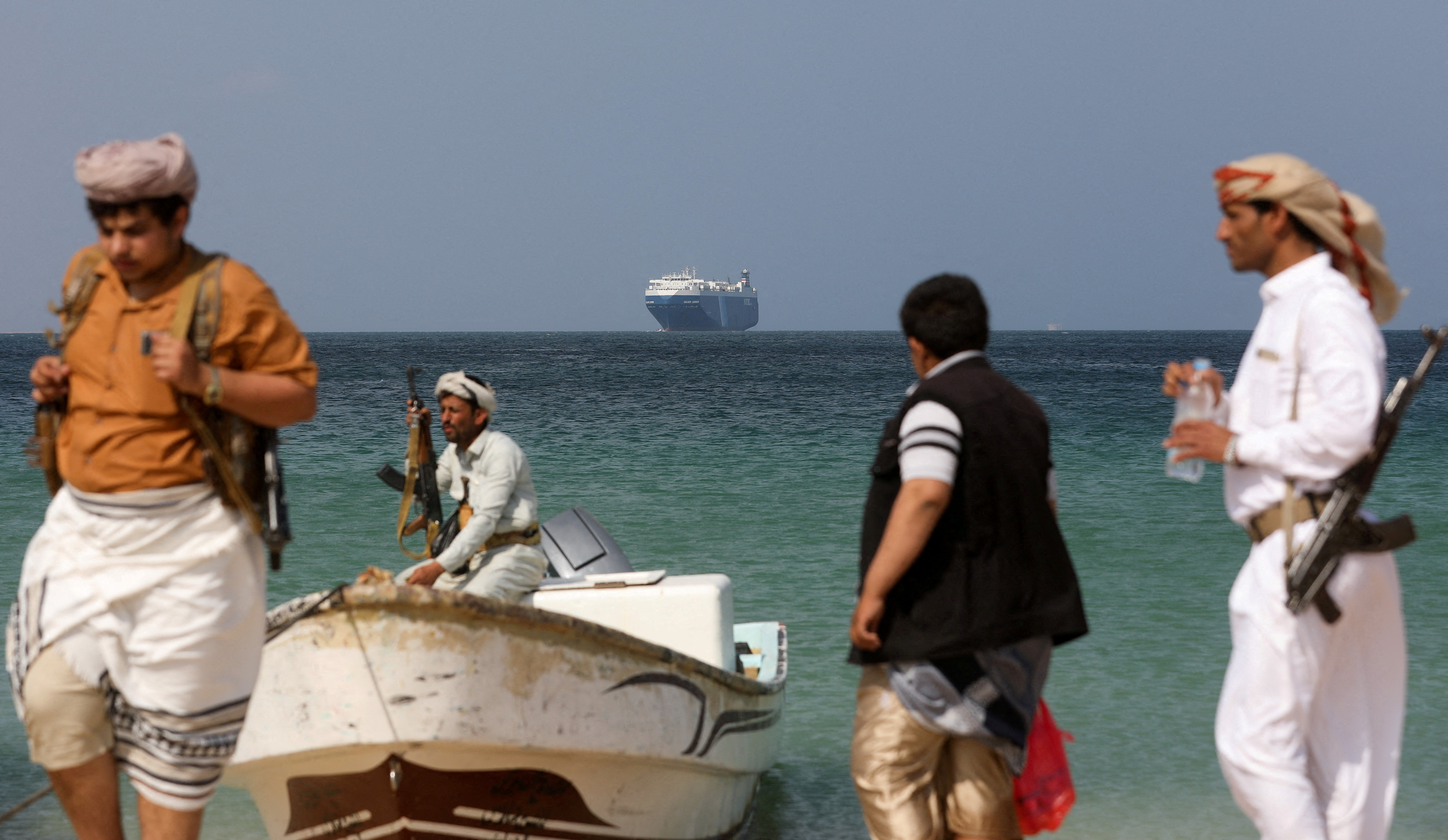 Armed men stand on the beach as the Galaxy Leader commercial ship,