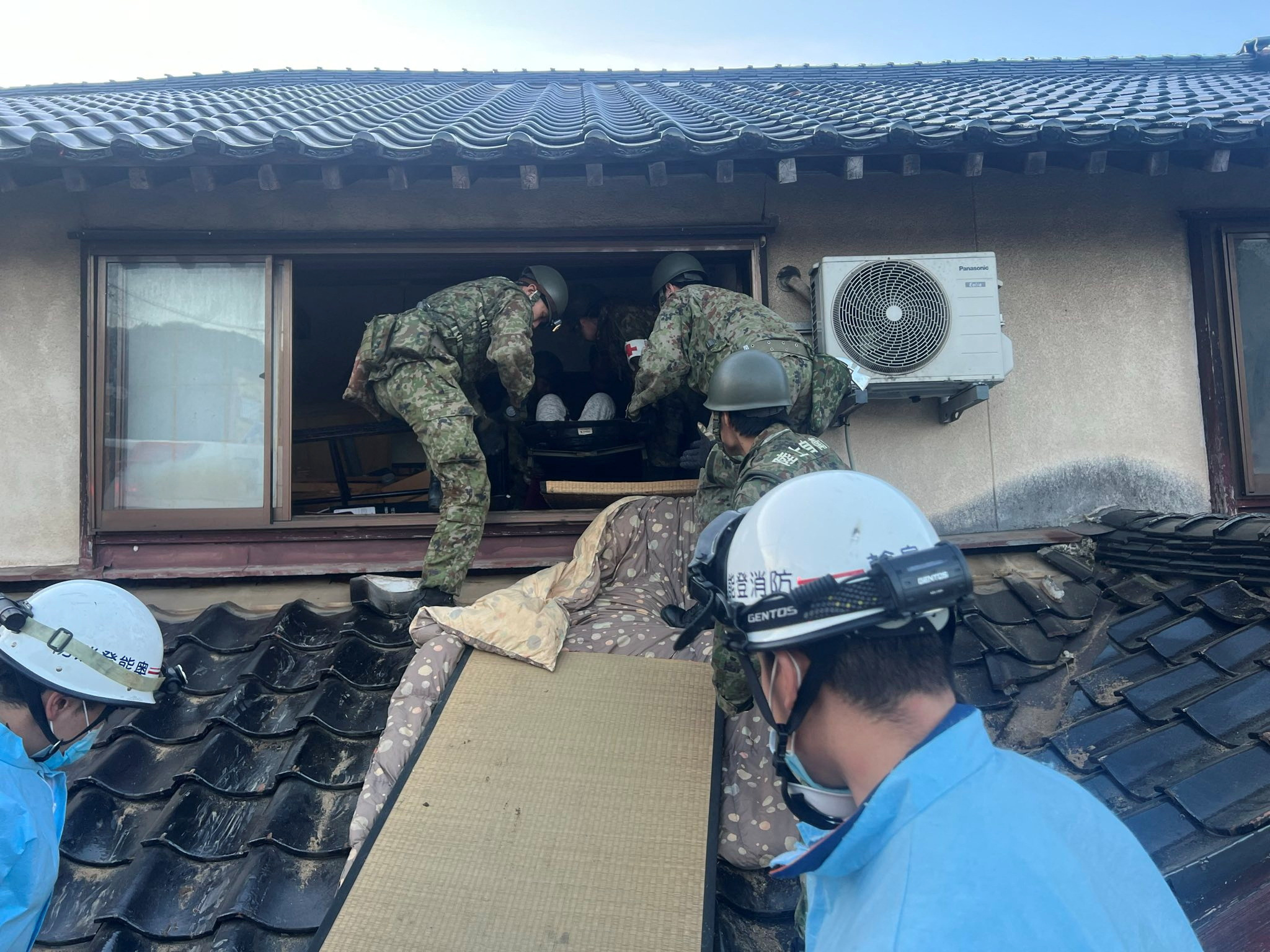 Two Japanese soldiers trying to bring someone out from the upper floor of their wrecked home. 