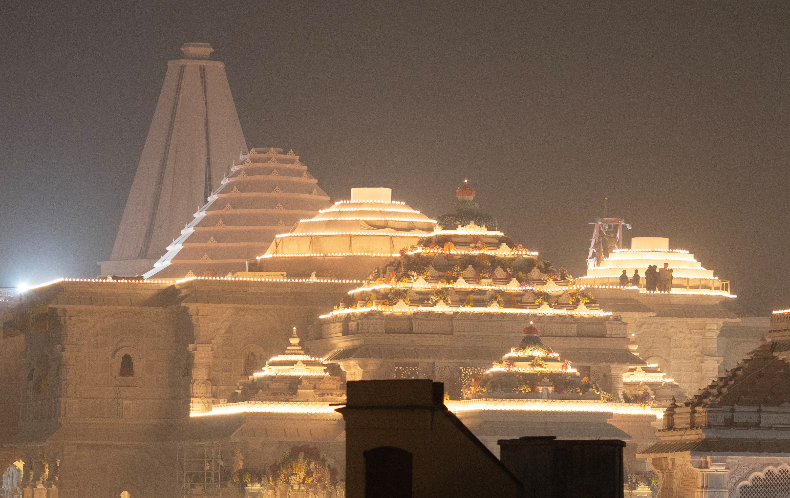 Labourers stand on top of the illuminated grand temple of Lord Ram ahead of its opening in Ayodhya in India, January 19, 2024. REUTERS/Adnan Abidi