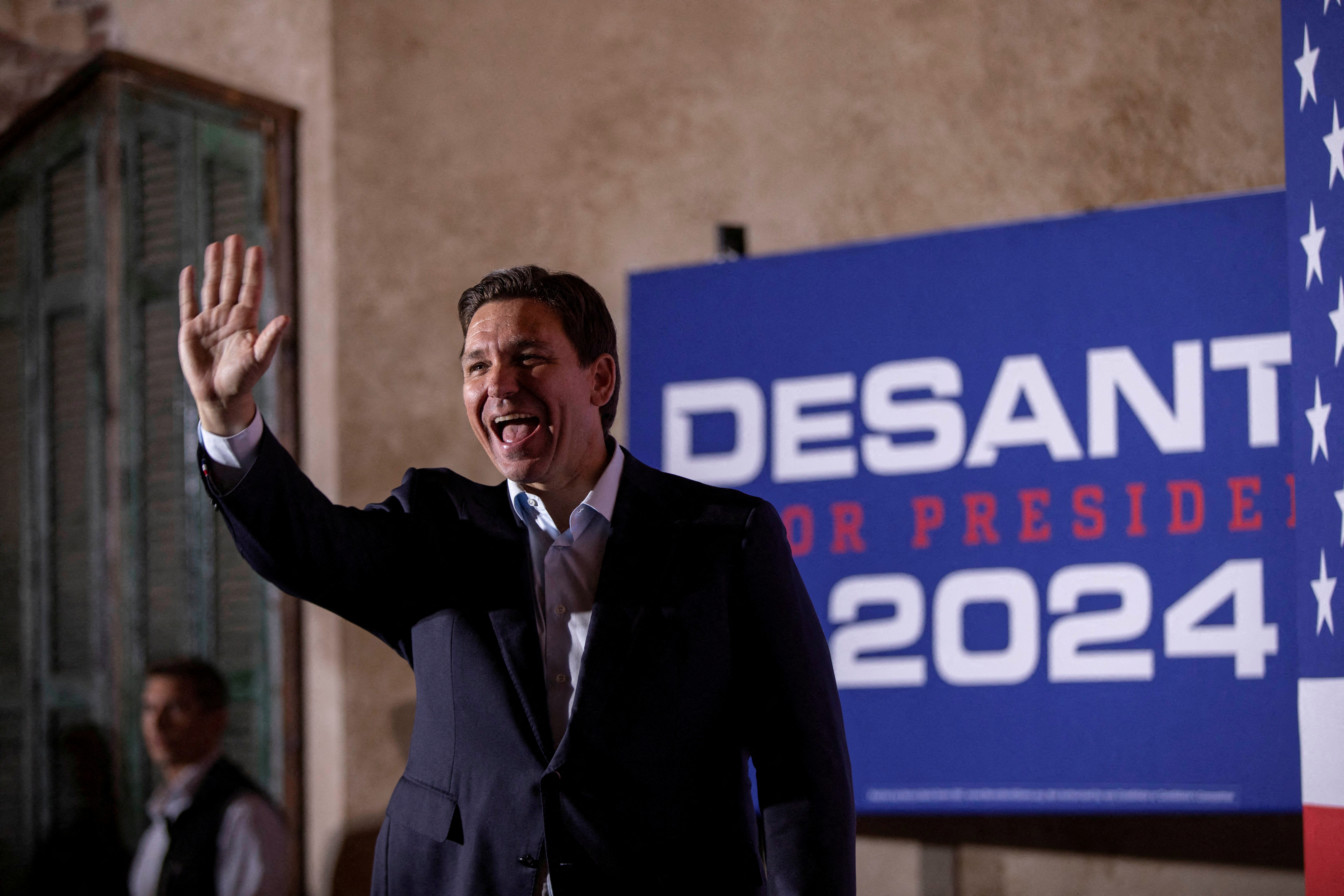 Ron DeSantis waving in front of a campaign poster