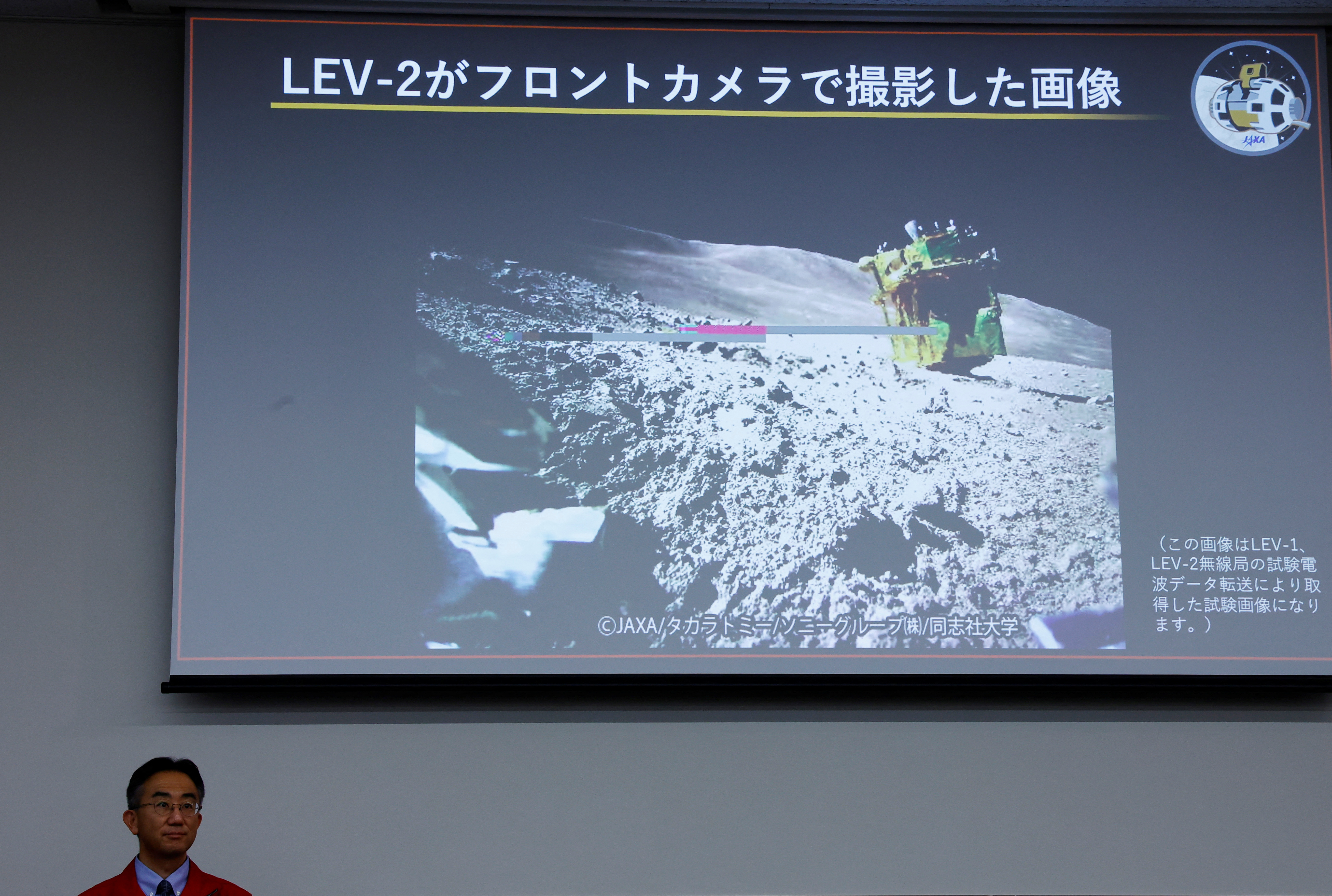 project team at the Japan Aerospace Exploration Agency (JAXA), sits in front of a screen projecting an image taken by LEV-2 on the moon, during a press conference