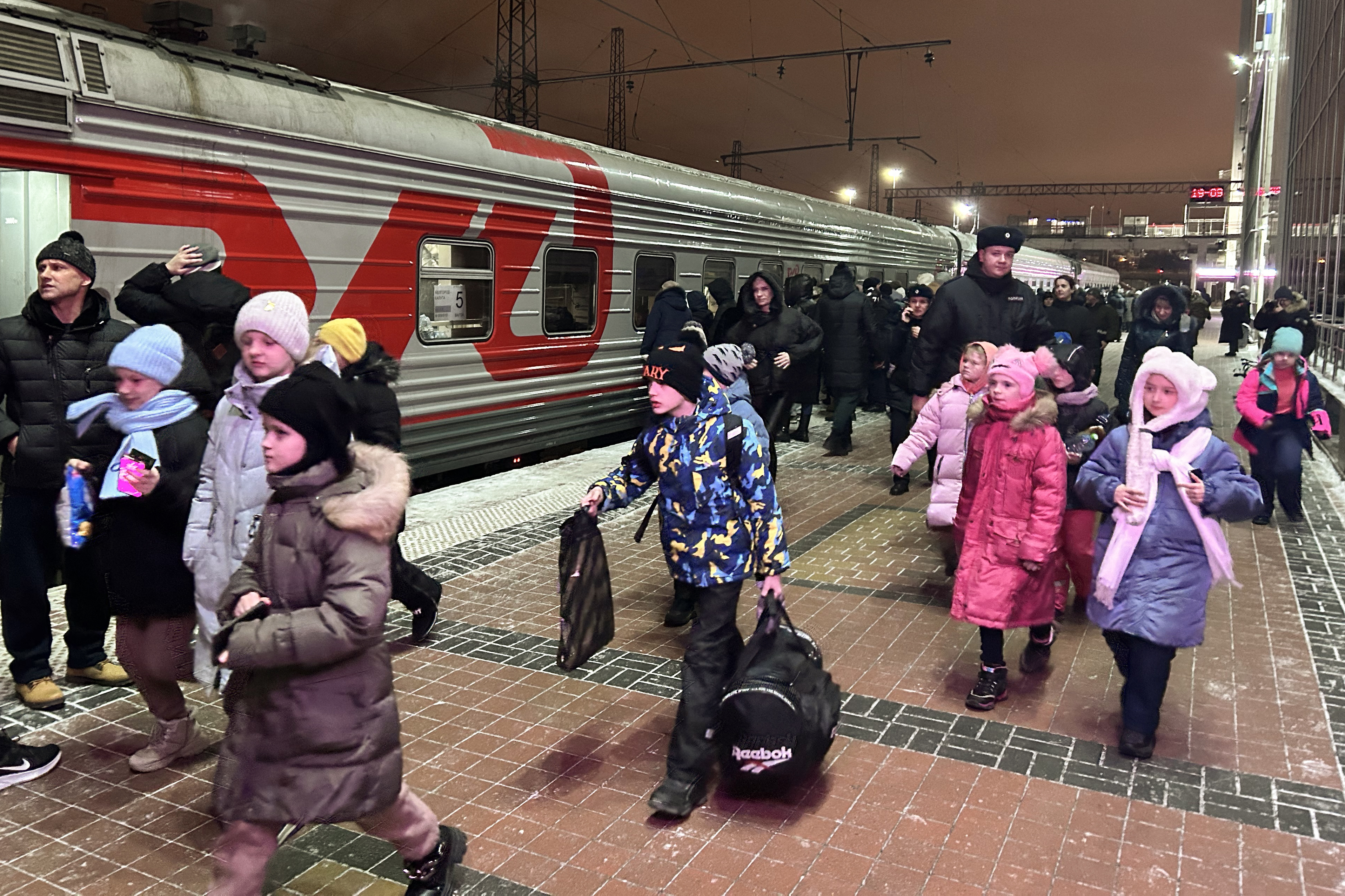 Children boarding a train. They are wearing colourful jackets and carrying bags.