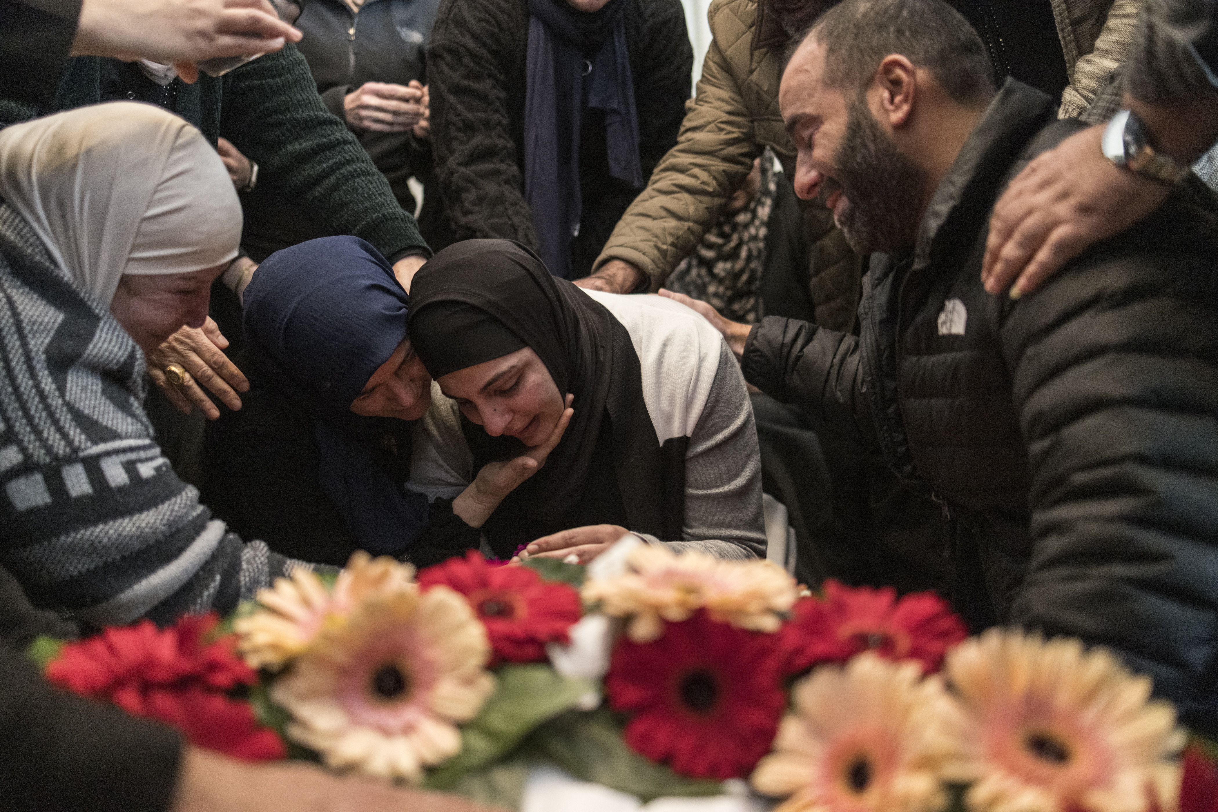 a grieving family surround a body covered in flowers