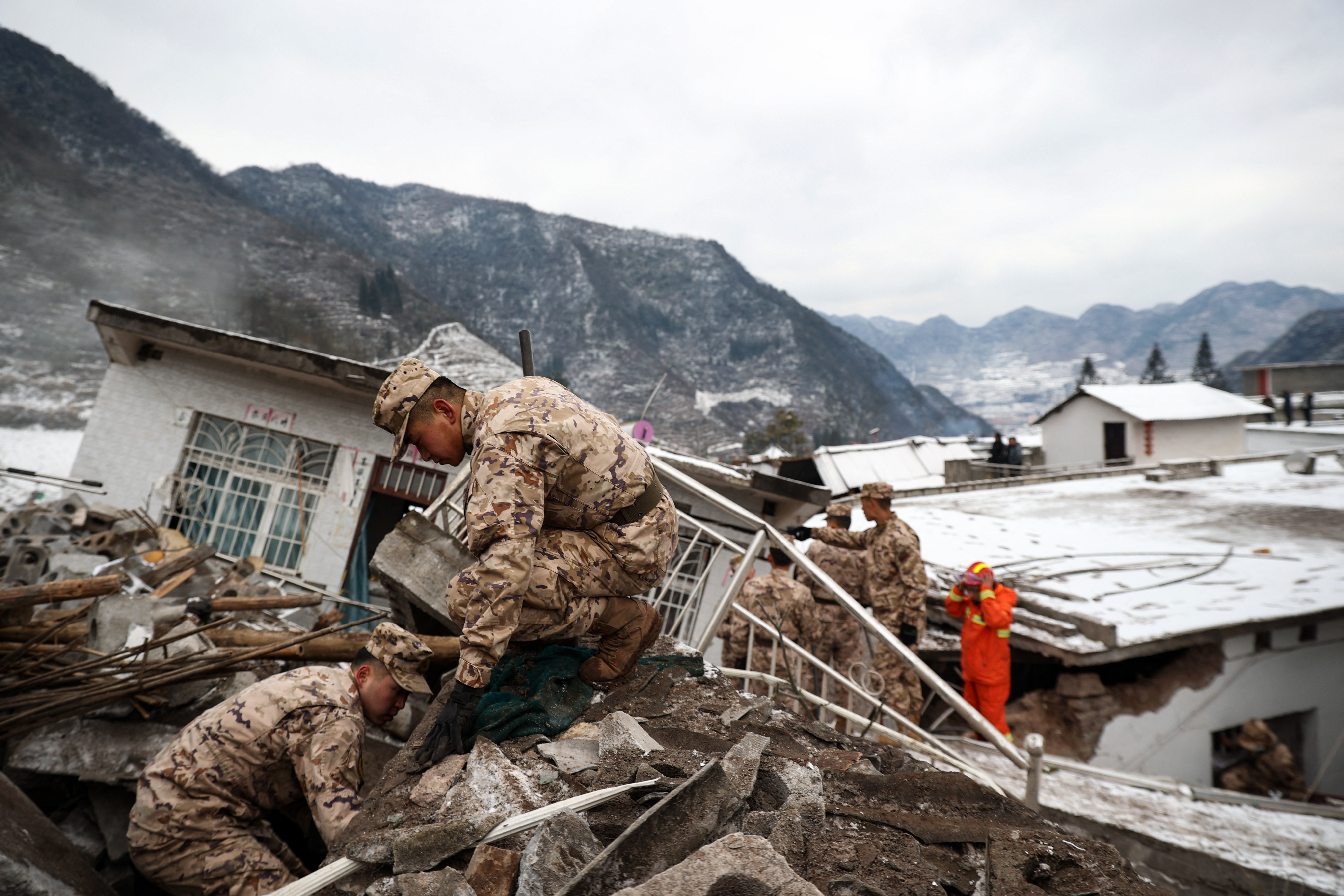 Soldiers involved in rescue efforts, Steep mountains are behind. They are dusted with snow.