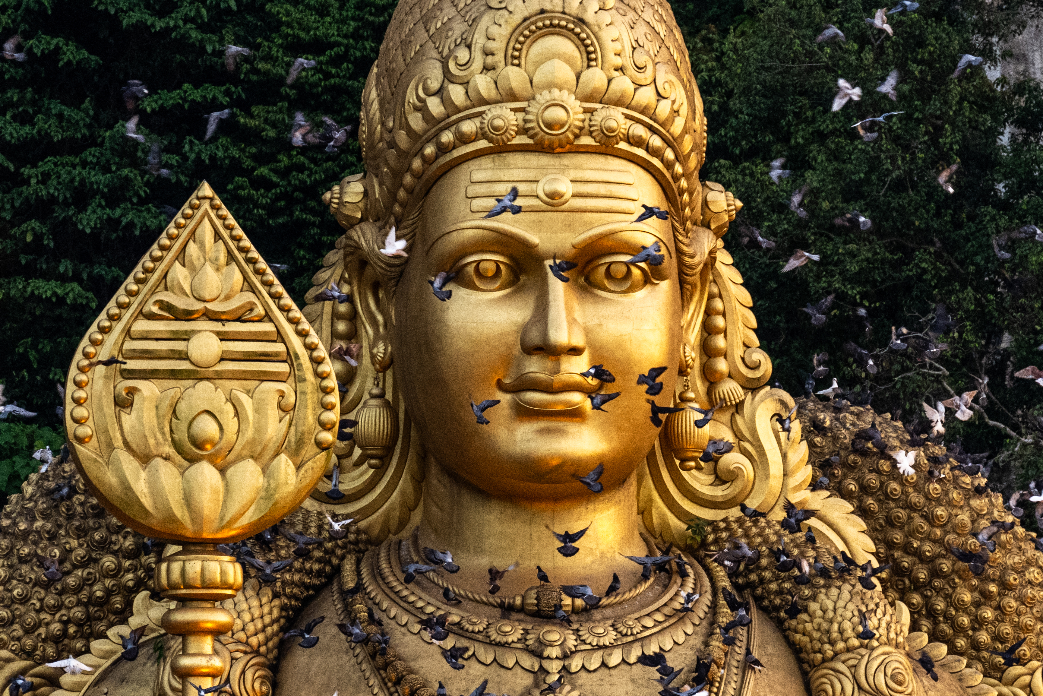 The golden statue of Lord Murugan at Batu Caves in Malaysia. Pigeons are flying in front.