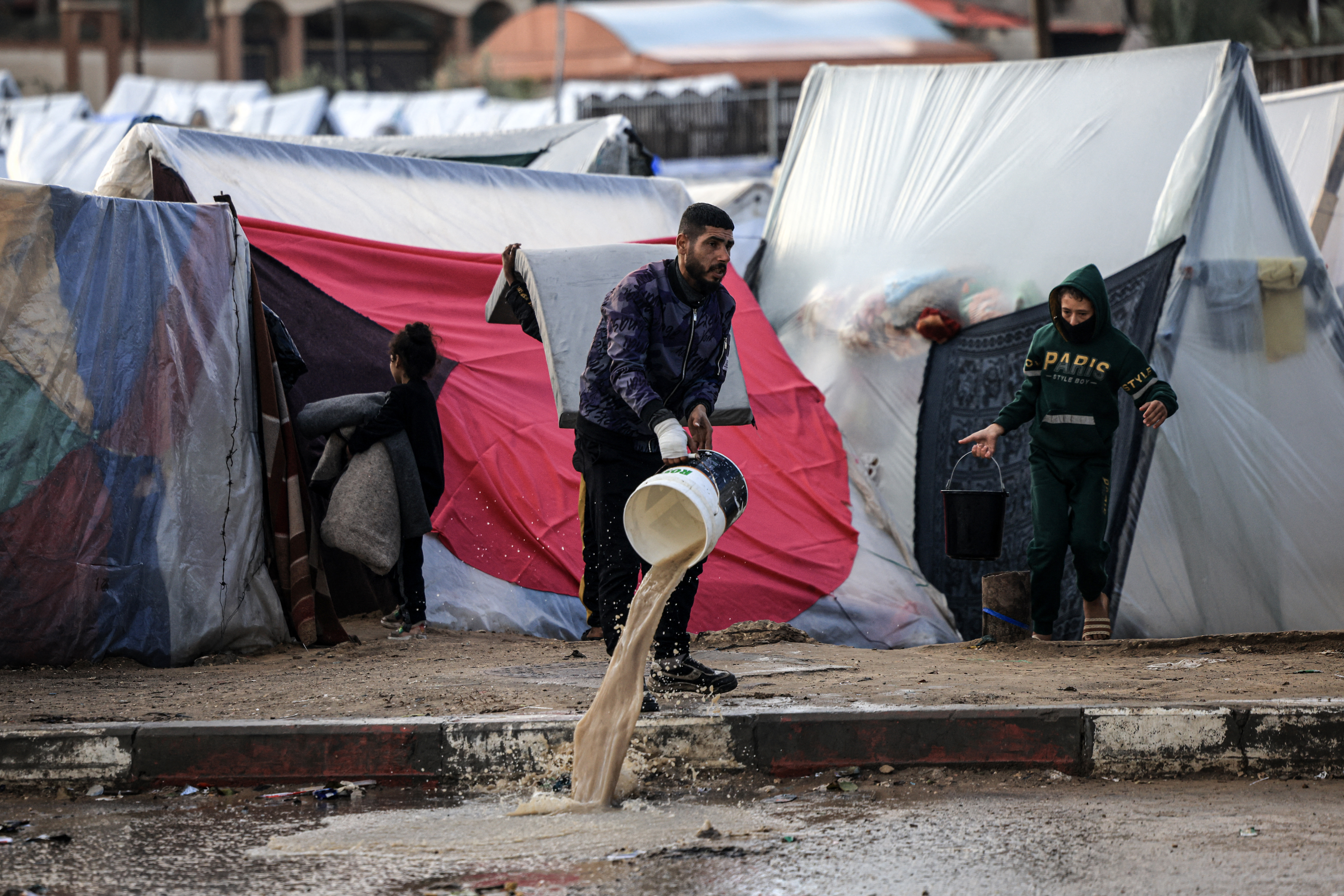 A displaced Palestinian uses a bucket to clear water from a tent drenched by heavy rain