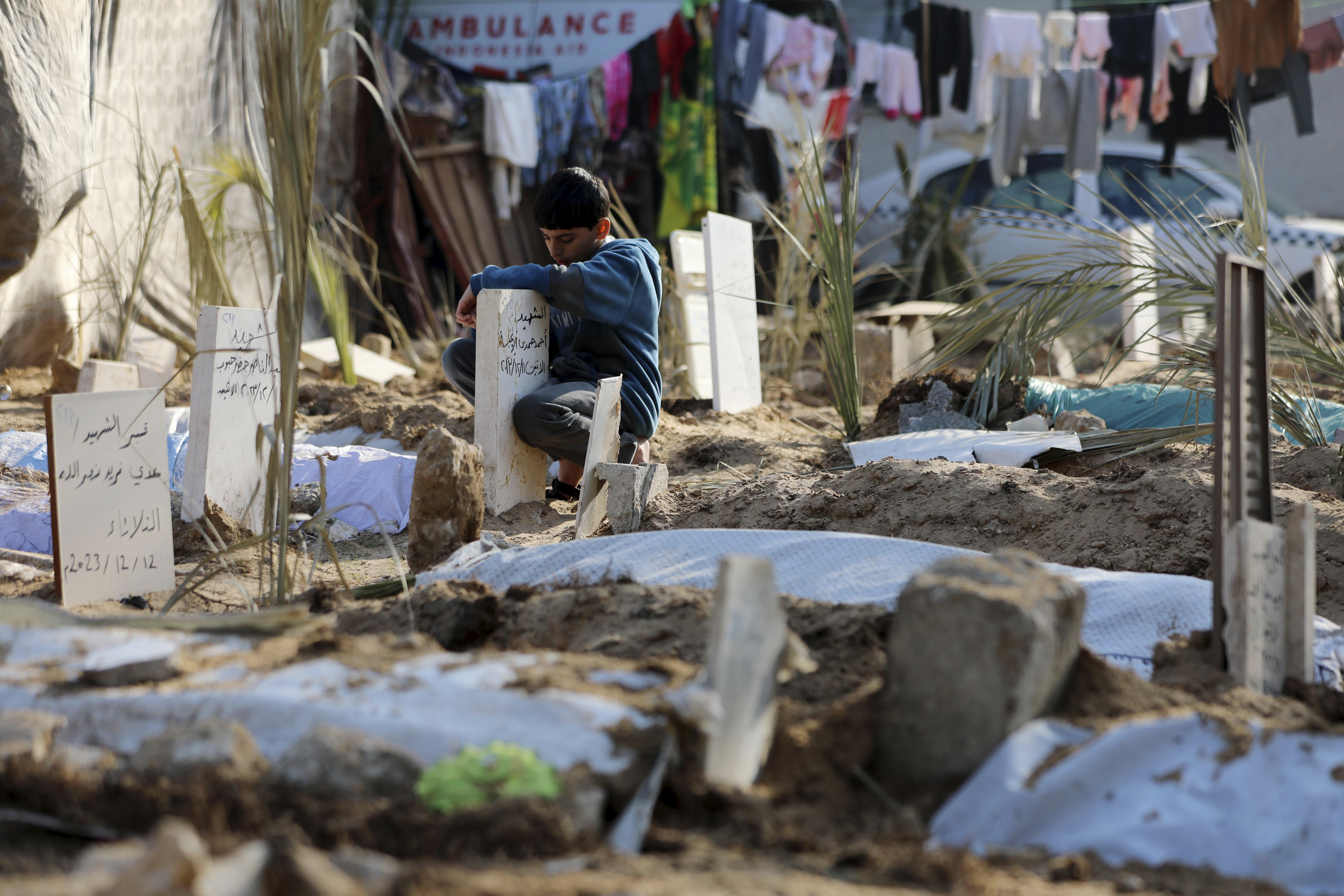A Palestinian child clings to a grave among those of people killed in the Israeli bombardment of Gaza City, on Sunday, December 31, 2023 [Mohammed Hajjar/AP]