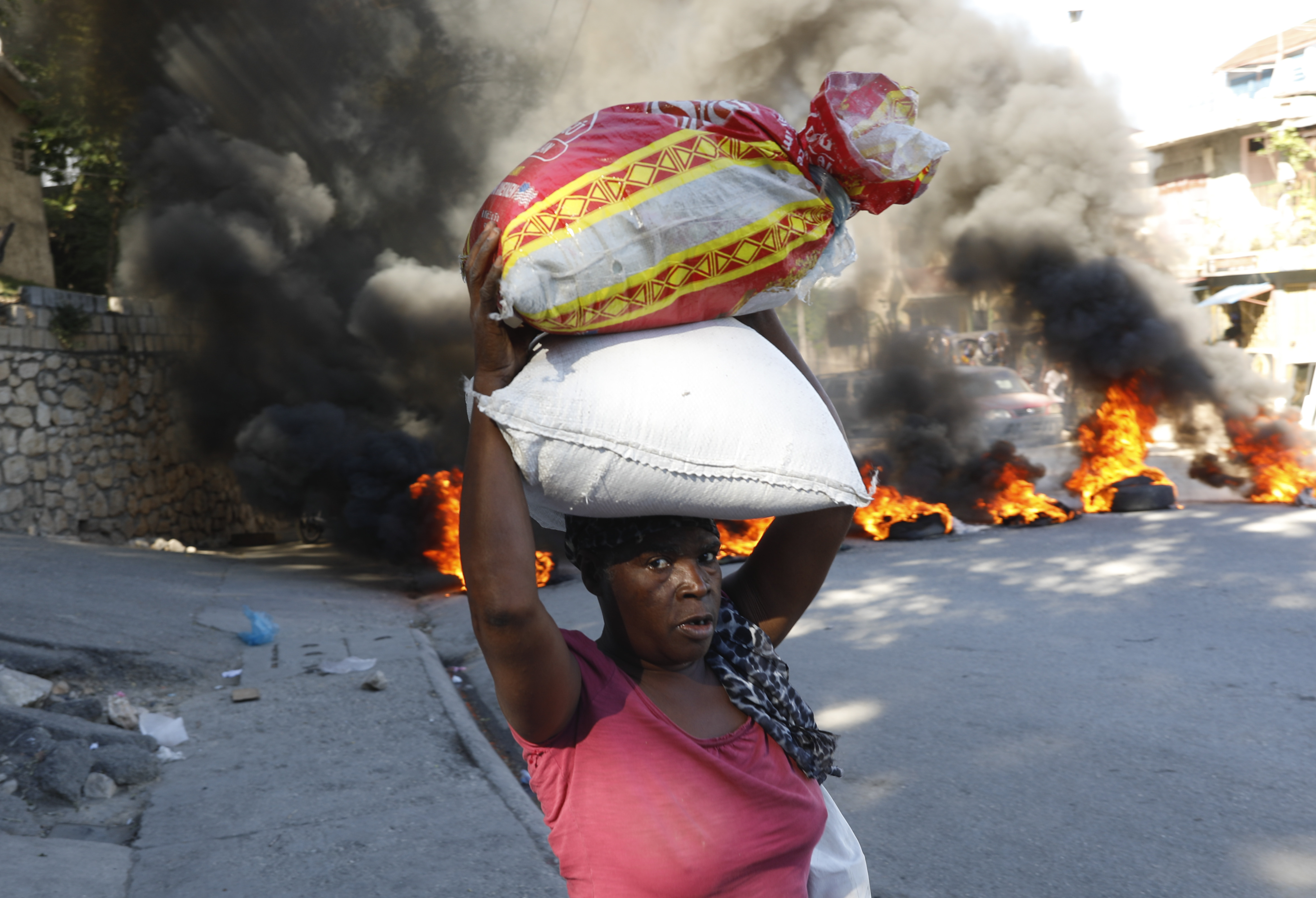 A woman walks past burning tires set on fire by protesters to call attention to the country's insecurity and demanding the resignation of the prime minister, in Port-au-Prince, Haiti, Thursday, Jan. 18