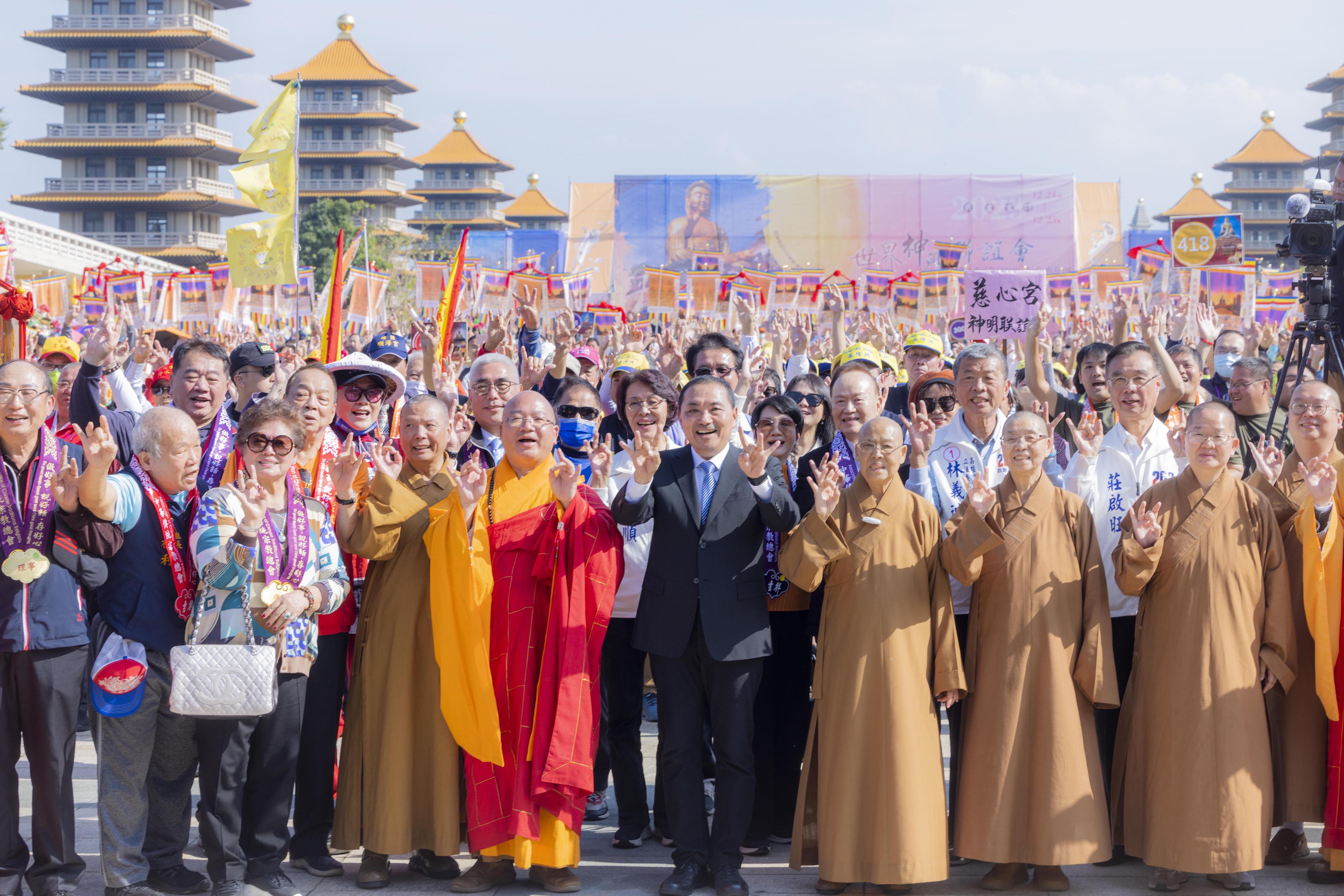 Hou Yu-ih at Buddha Light Mountain in December. He is standing outside with the temple's monks around him and a hue crowd behind. Pagodas can also be seen in the background.