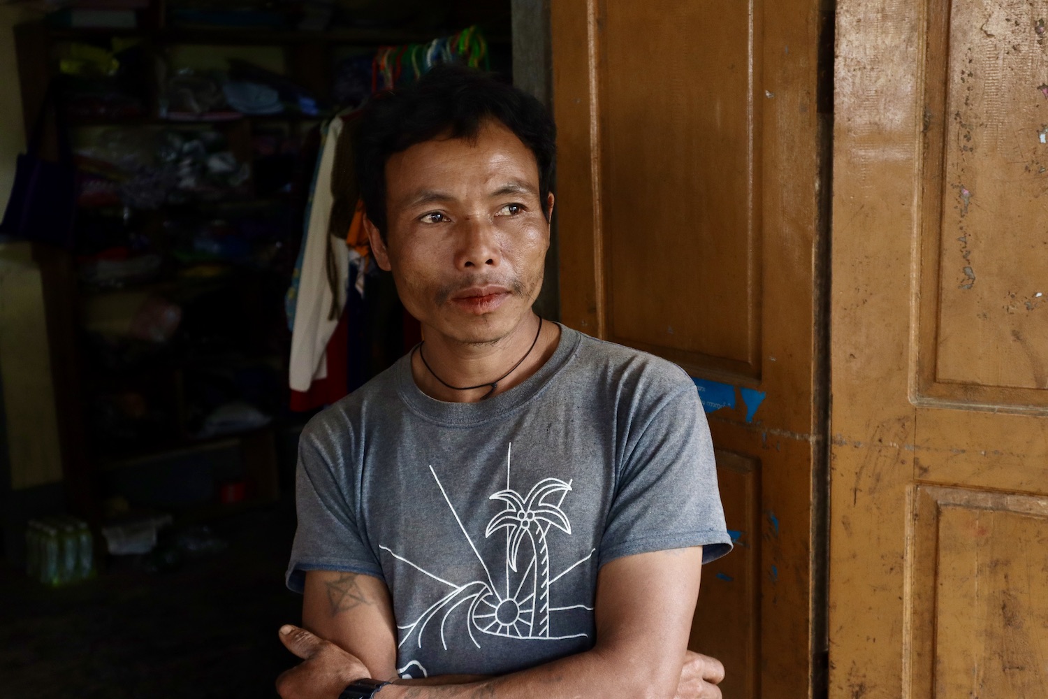  Nwe Lay, He is seated by a wooden door.