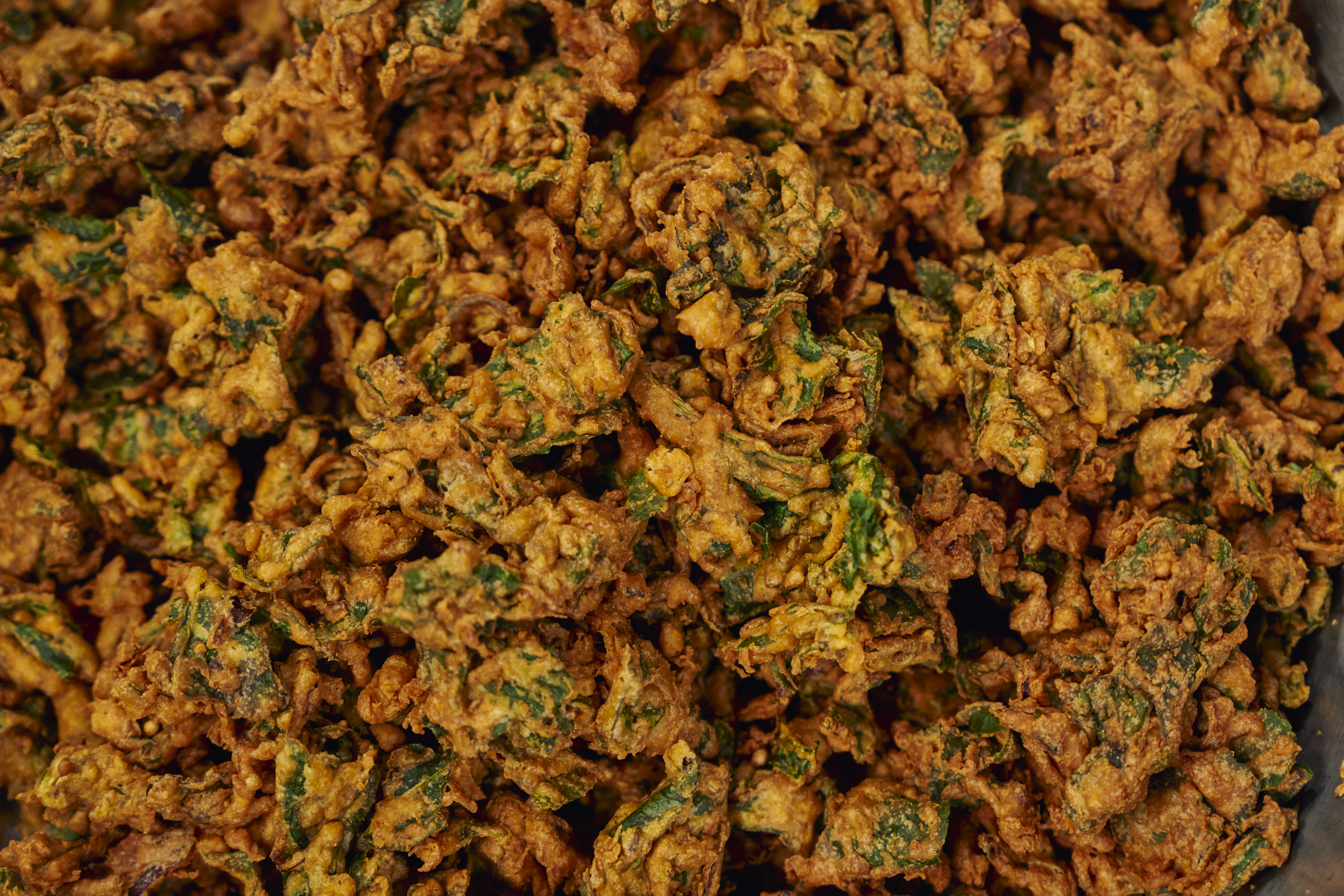 Fried pakodas from the Khalsa Diwan Sikh Temple kitchen in Manila, Philippines A large pot of saag simmers as a volunteer uses a large drill to stir the dish thoroughly [Sonny Thakur/Al Jazeera]