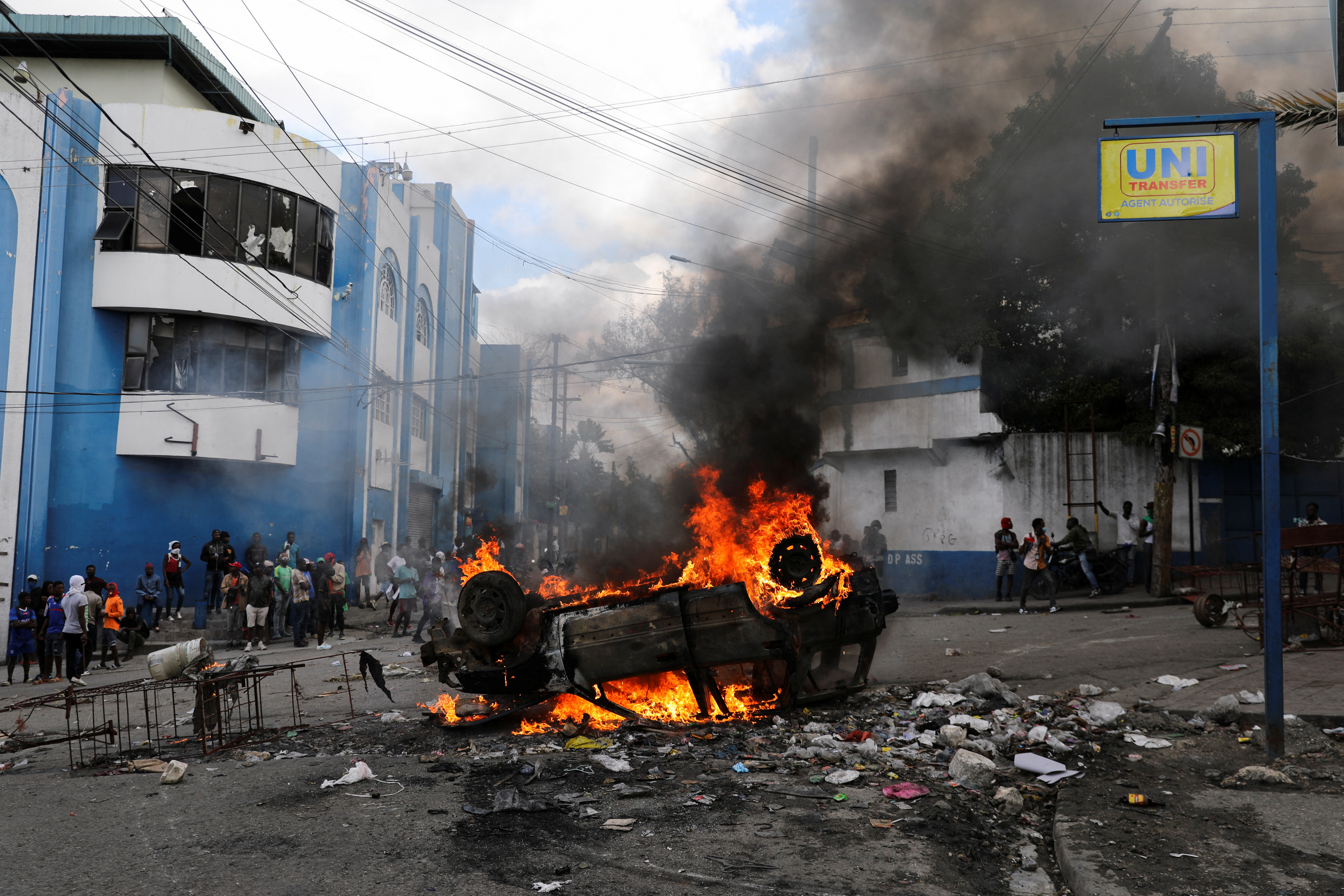 People stand near a car set ablaze by demonstrators