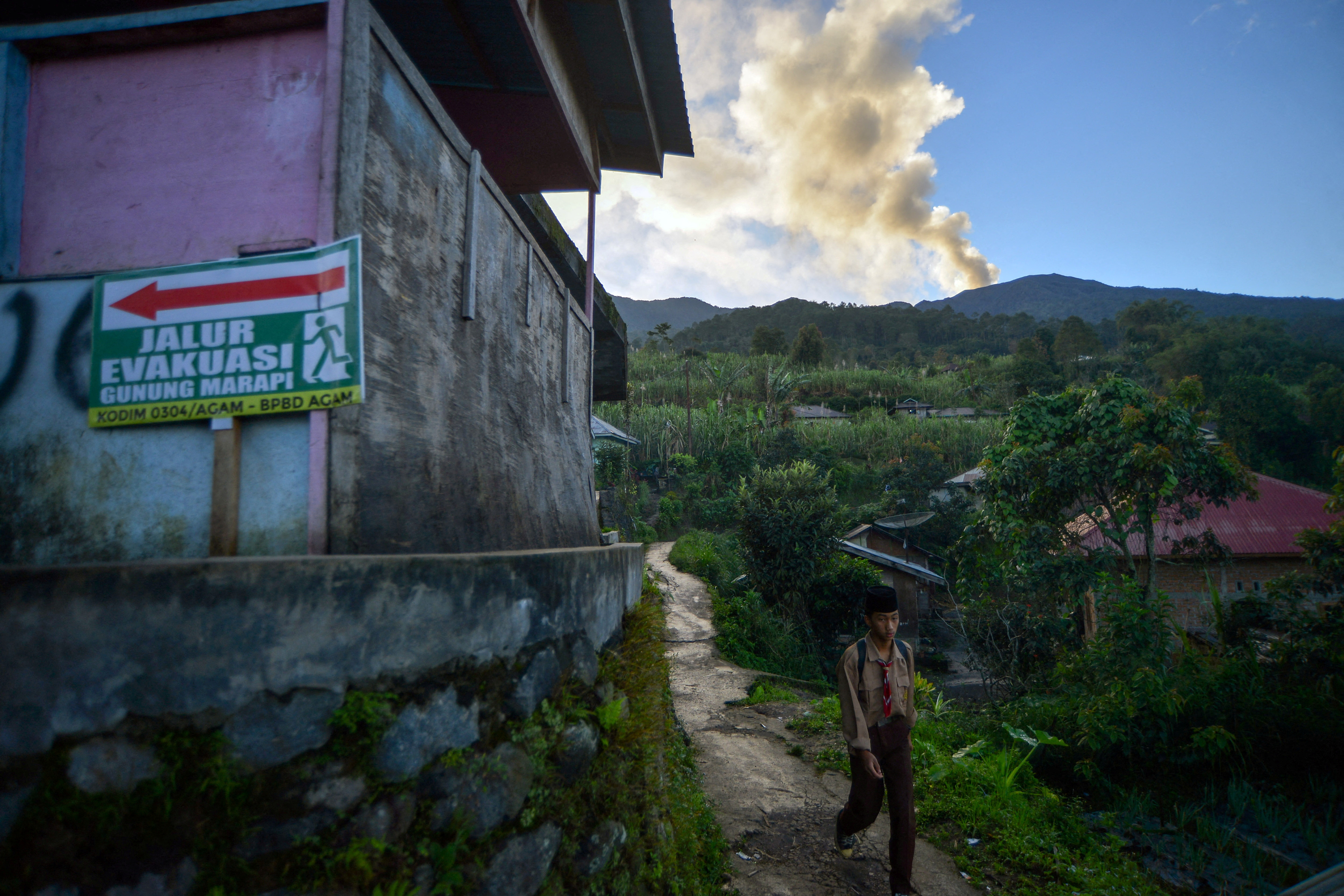 A student walks past as Mount Marapi spews ash, seen from Jorong Batang Silasiah in Agam, West Sumatra province, Indonesia