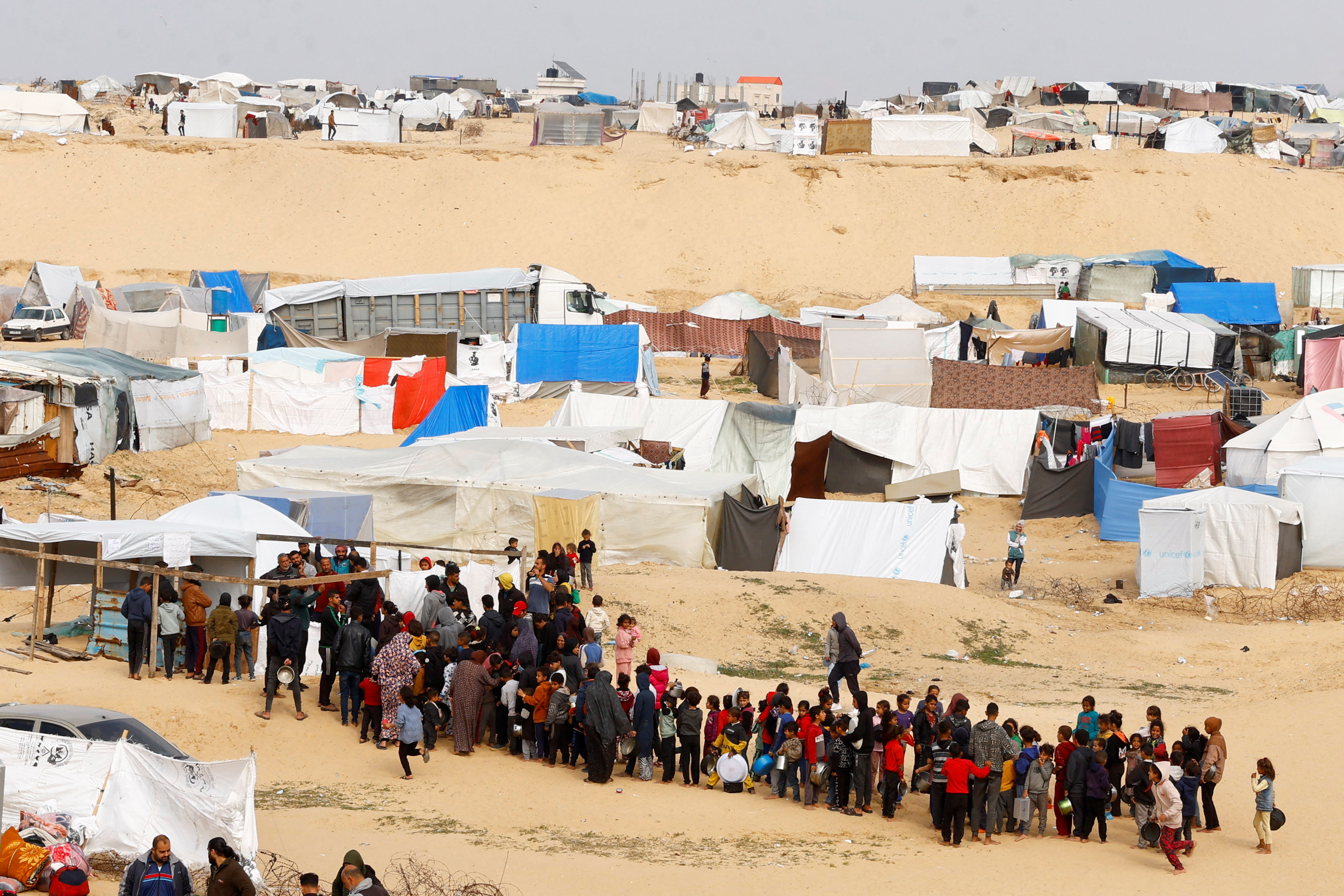 Displaced Palestinians wait to receive free food at a tent camp, amid food shortages