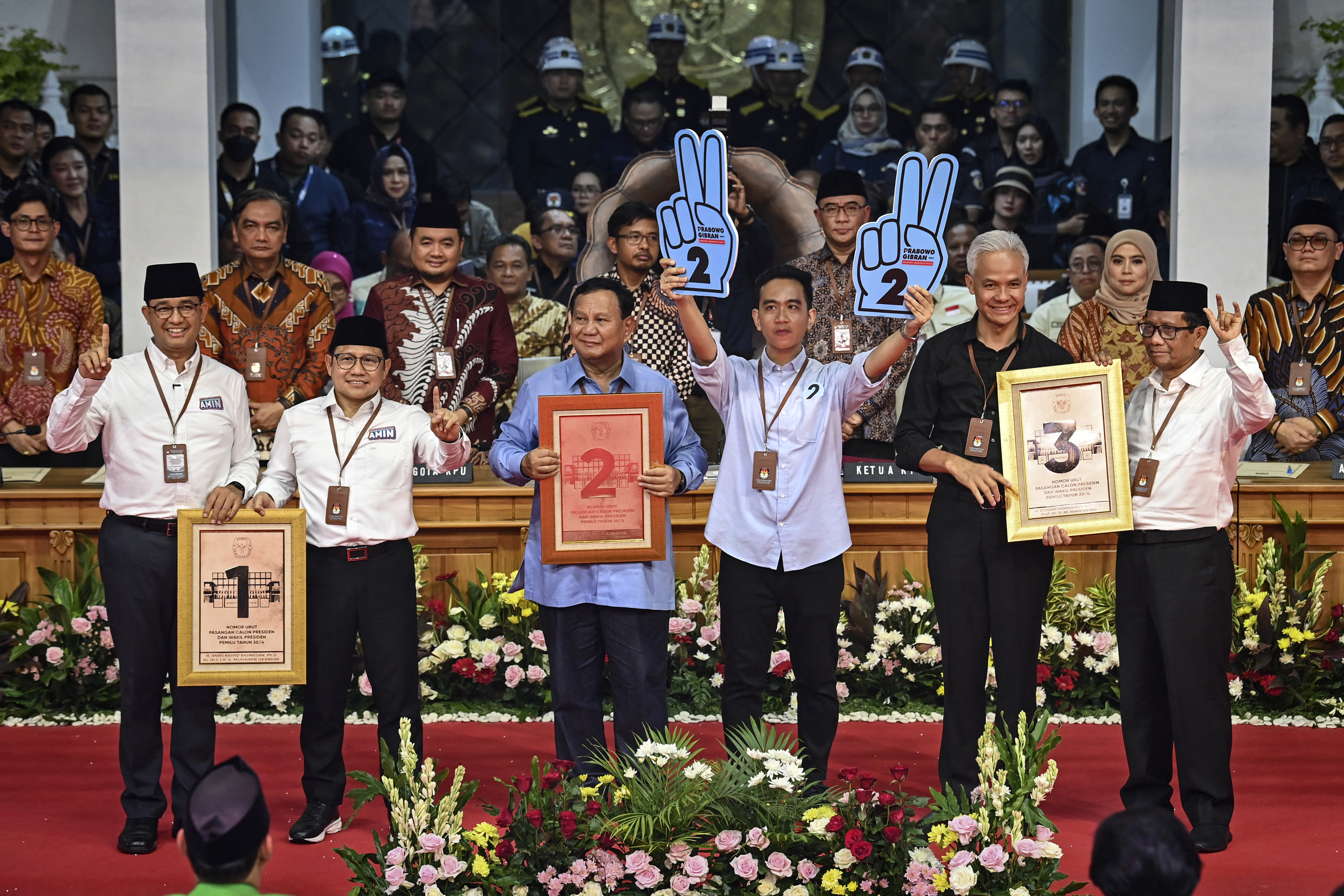 The presidential candidates with their running mates. They are holding up placards with their candidate numbers - 1, 2 and 3. Gibran is holding up two pale blue hands with the number two written on them.