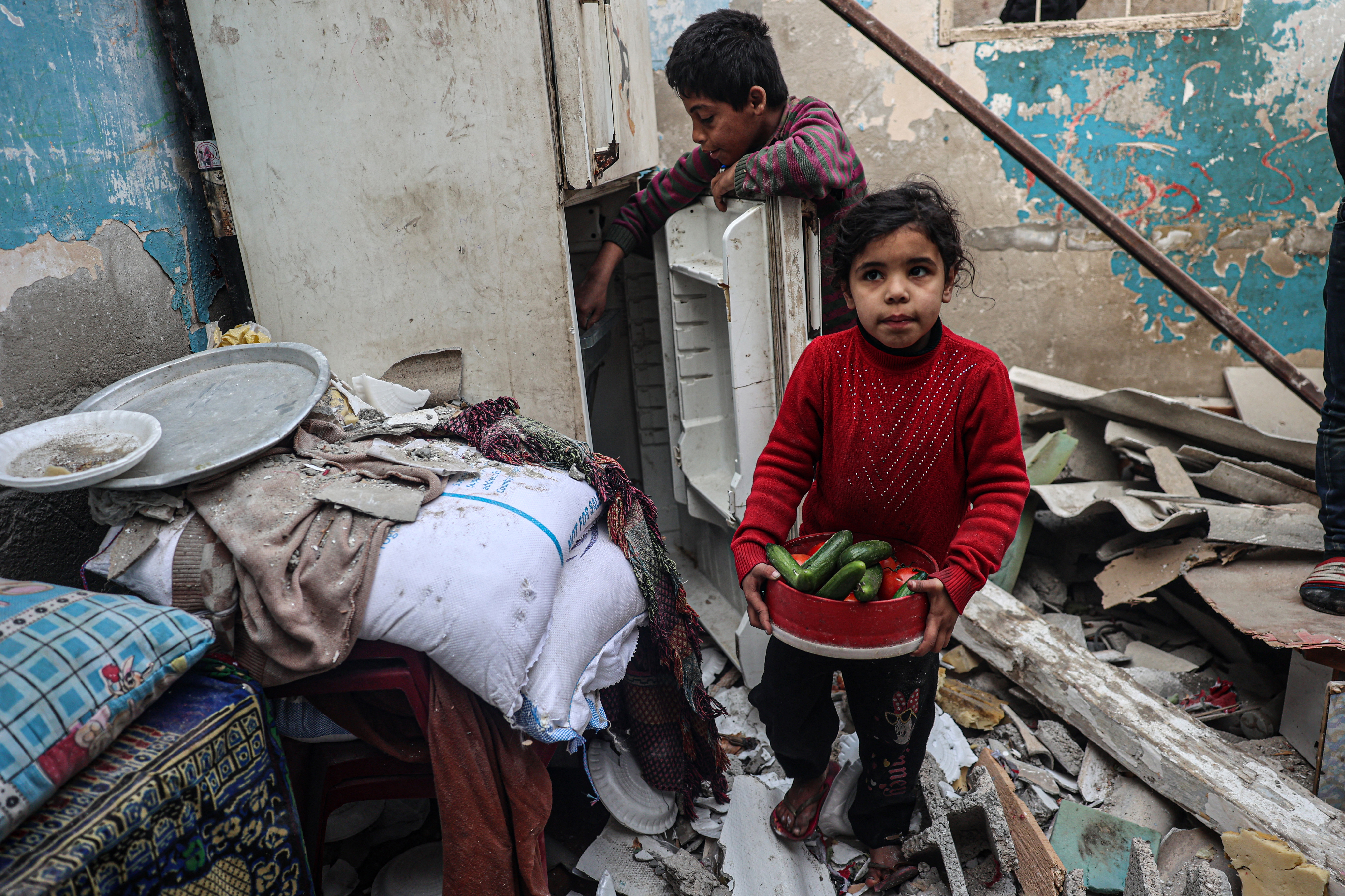 A child carries food items as another tries to salvage more from a refrigerator inside their damaged home, following overnight Israeli bombardment in Rafah in the southern Gaza Strip on February 25