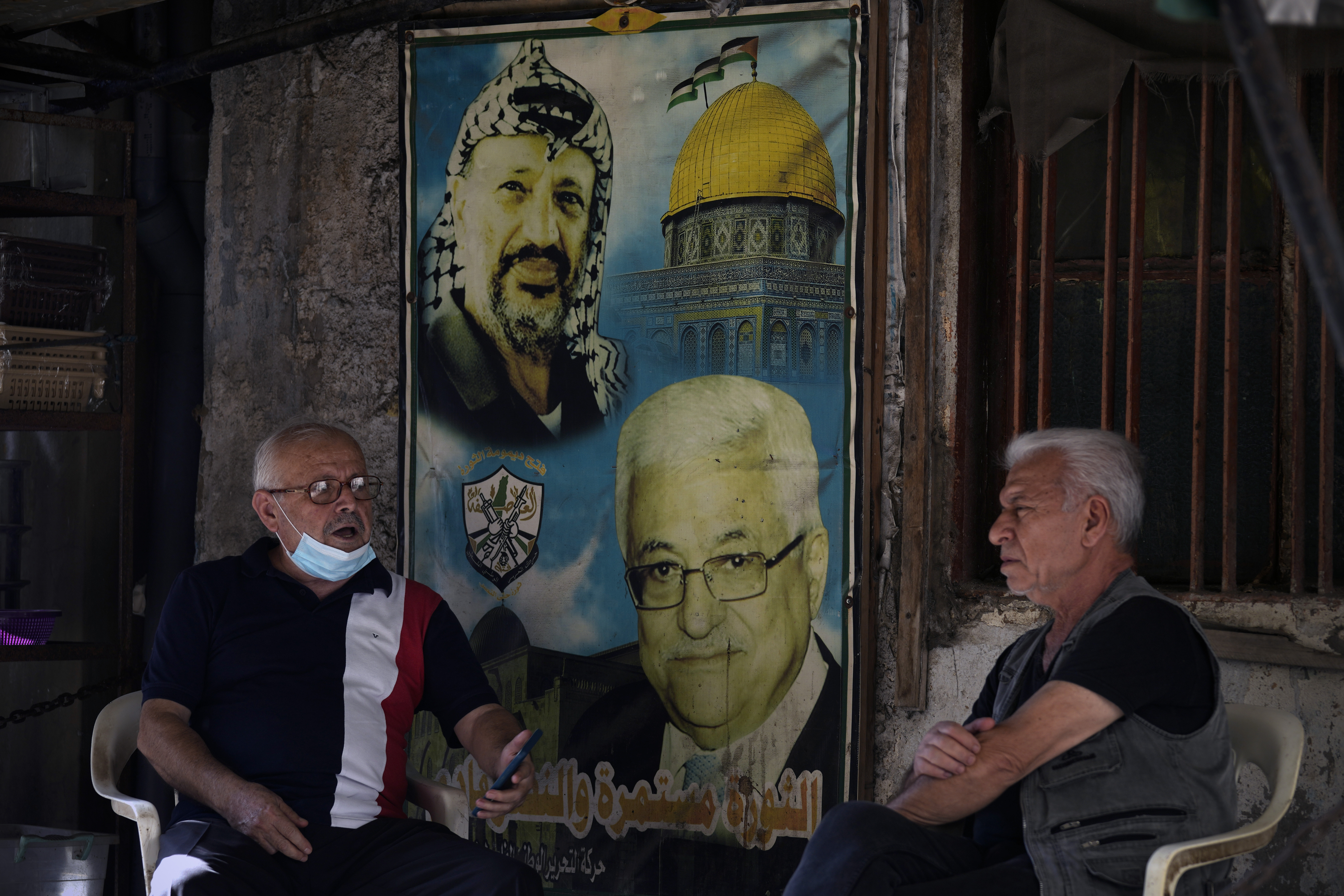 Palestinians speak as they sit next to a poster of the late Palestinian leader Yasser Arafat, left, and Palestinian President Mahmoud Abbas, right, at the Bourj al-Barajneh Palestinian refugee camp, in Beirut, Lebanon, Friday, Oct. 21, 2022. Lebanon's historic economic meltdown is hard hitting Palestinian refugees in the small nation where the vast majority of them now live in poverty while others risk their lives in search for a better future abroad, the U.N. agency for Palestinian refugees said Friday. (AP Photo/Bilal Hussein)