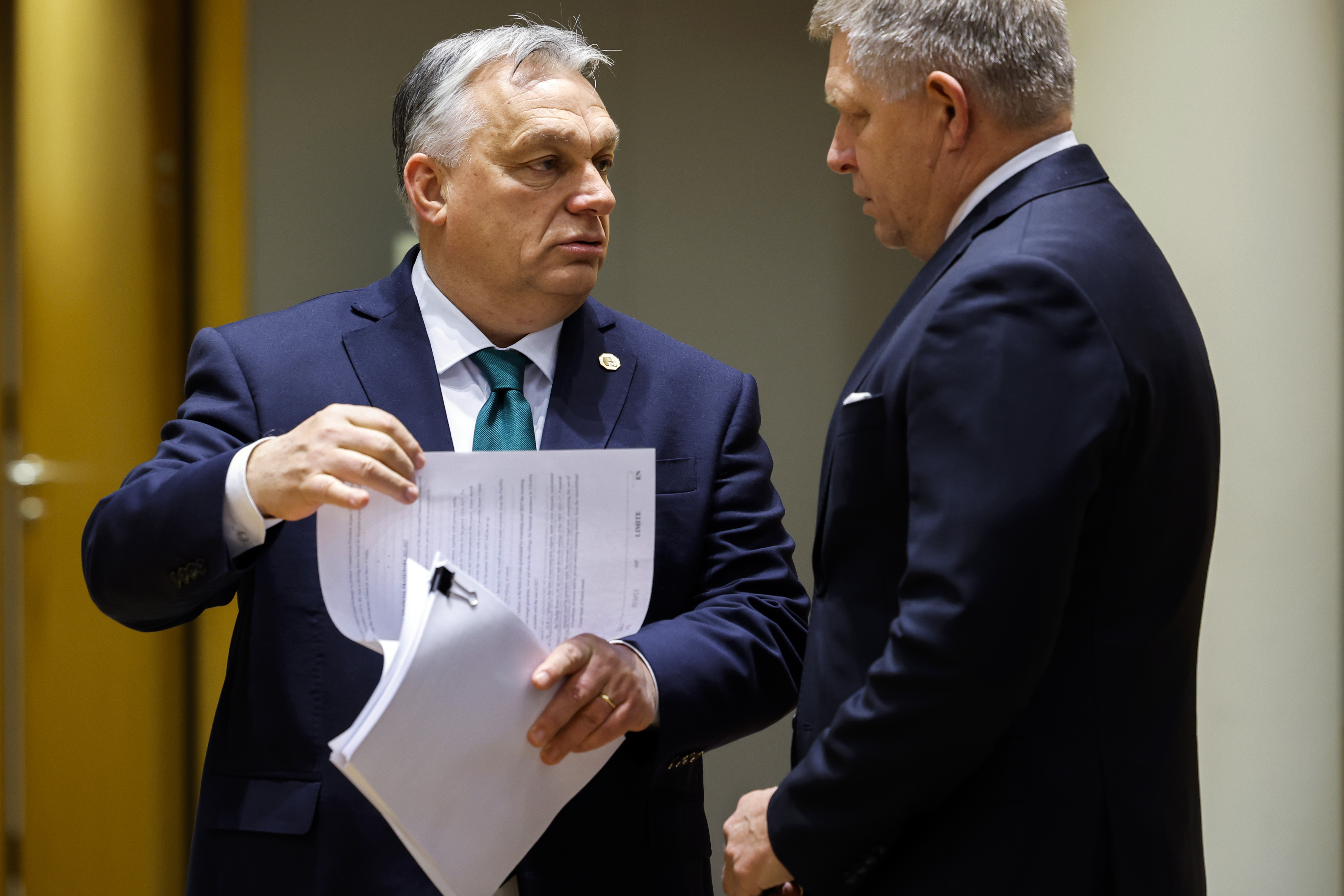 Victor Orban holds a packet of papers, lifting up one sheet while speaking to Robert Fico. Both men wear suits and ties.