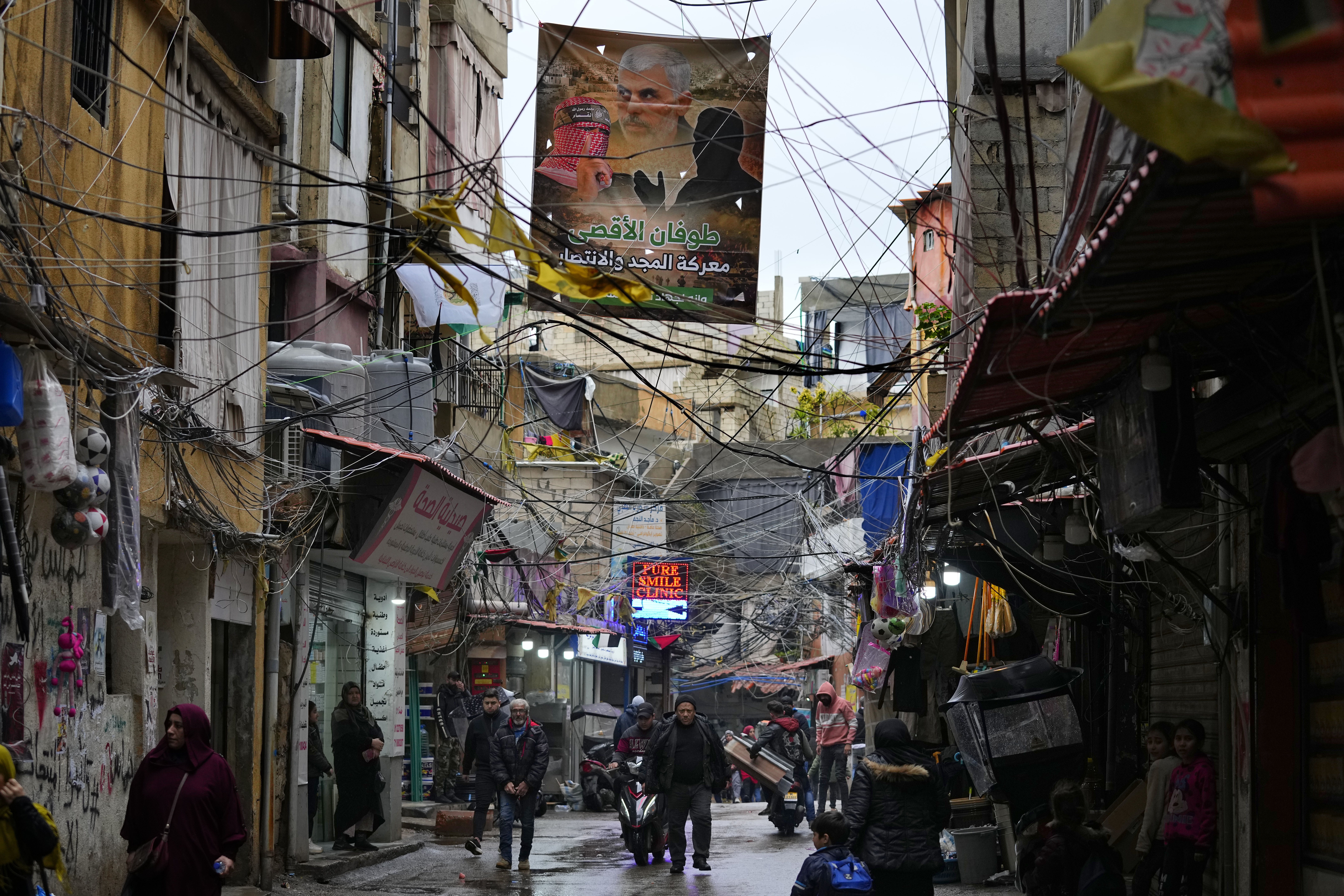 Palestinians walk under a poster that shows Yahya Sinwar, head of Hamas in Gaza, on a street inside the Bourj al-Barajneh Palestinian refugee camp, south of Beirut, Lebanon, Monday, Feb. 5, 2024. There are nearly 500,000 Palestinian refugees registered in Lebanon, although the actual number in the country is believed to be around 200,000, as many have emigrated but remain on UNRWA's roster. (AP Photo/Bilal Hussein)