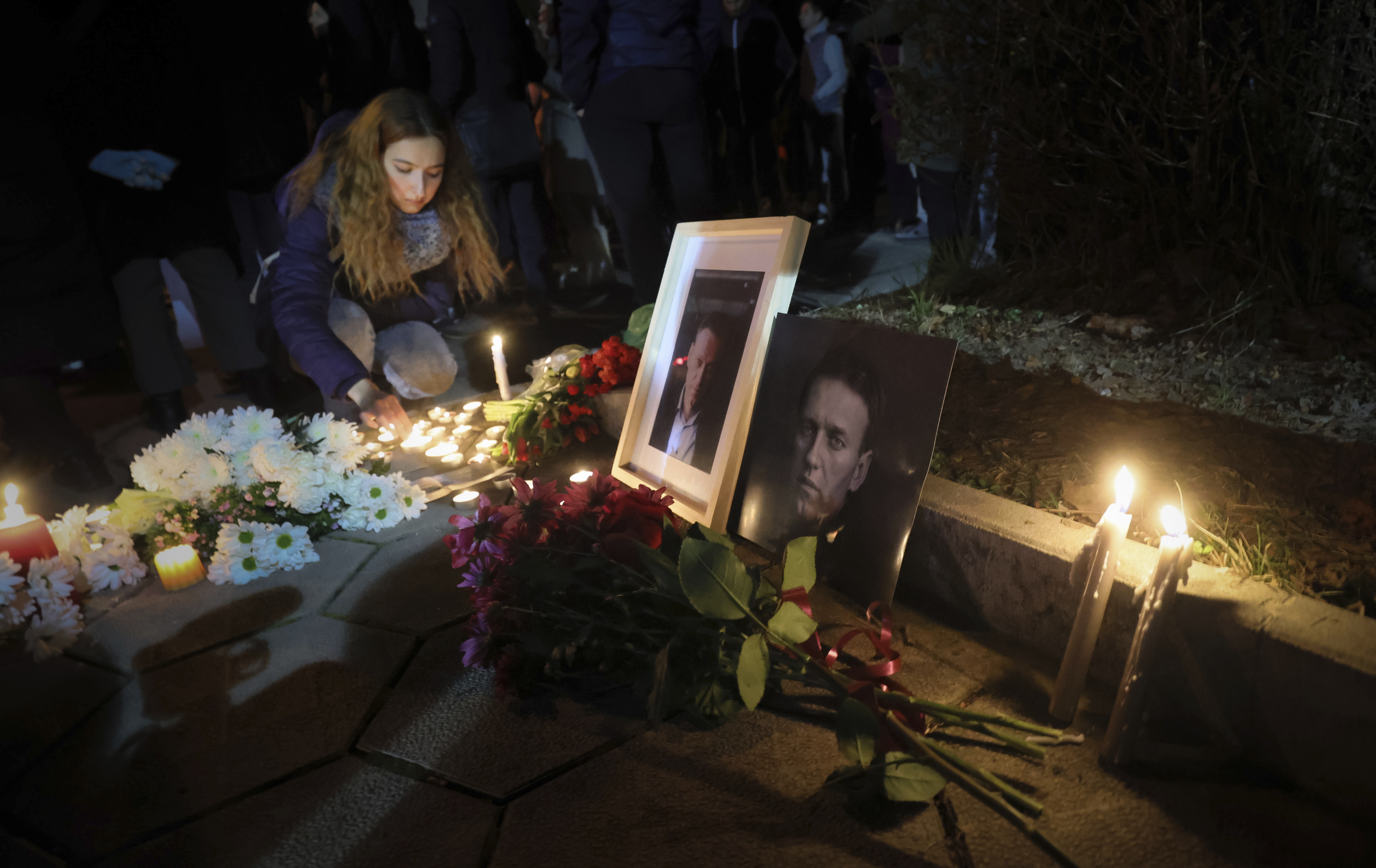 A woman lights a candle as portraits of Alexei Navalny, candles and flowers are laid in front of Russian embassy in Sofia, Bulgaria