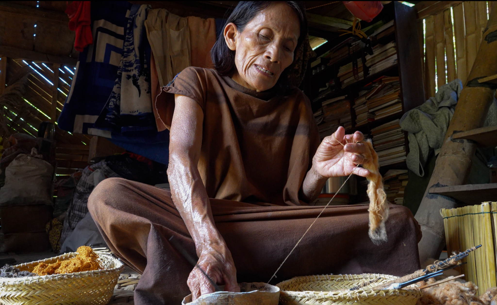 A woman sits cross-legged and spins cotton from raw materials.