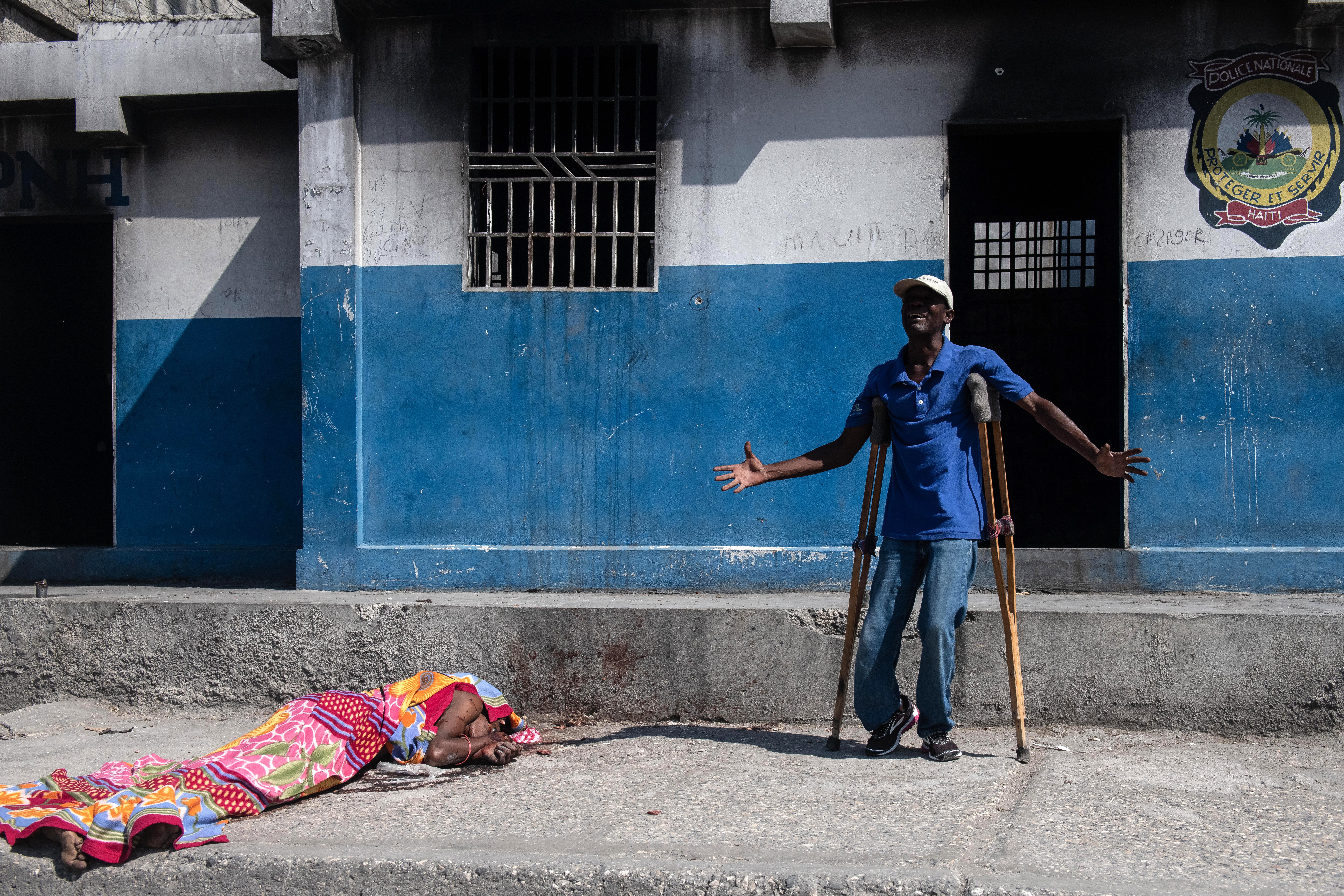 A man cries next to the lifeless body of a person outside the Carrefour Aeroport police station