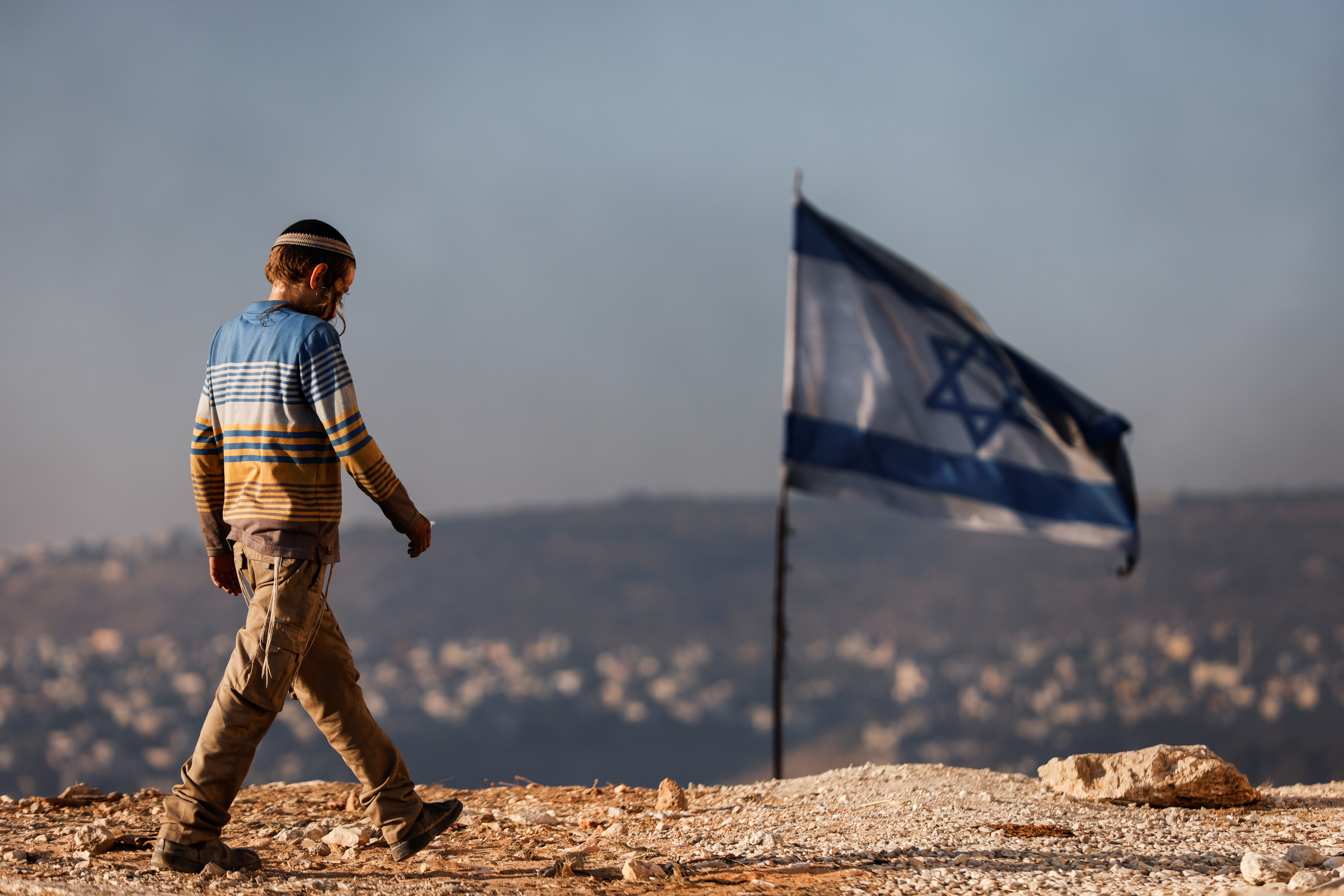A Jewish settler teenager walks by an Israeli flag in Givat Eviatar, a new Israeli settler outpost, near the Palestinian village of Beita in the Israeli-occupied West Bank June 23, 2021.
