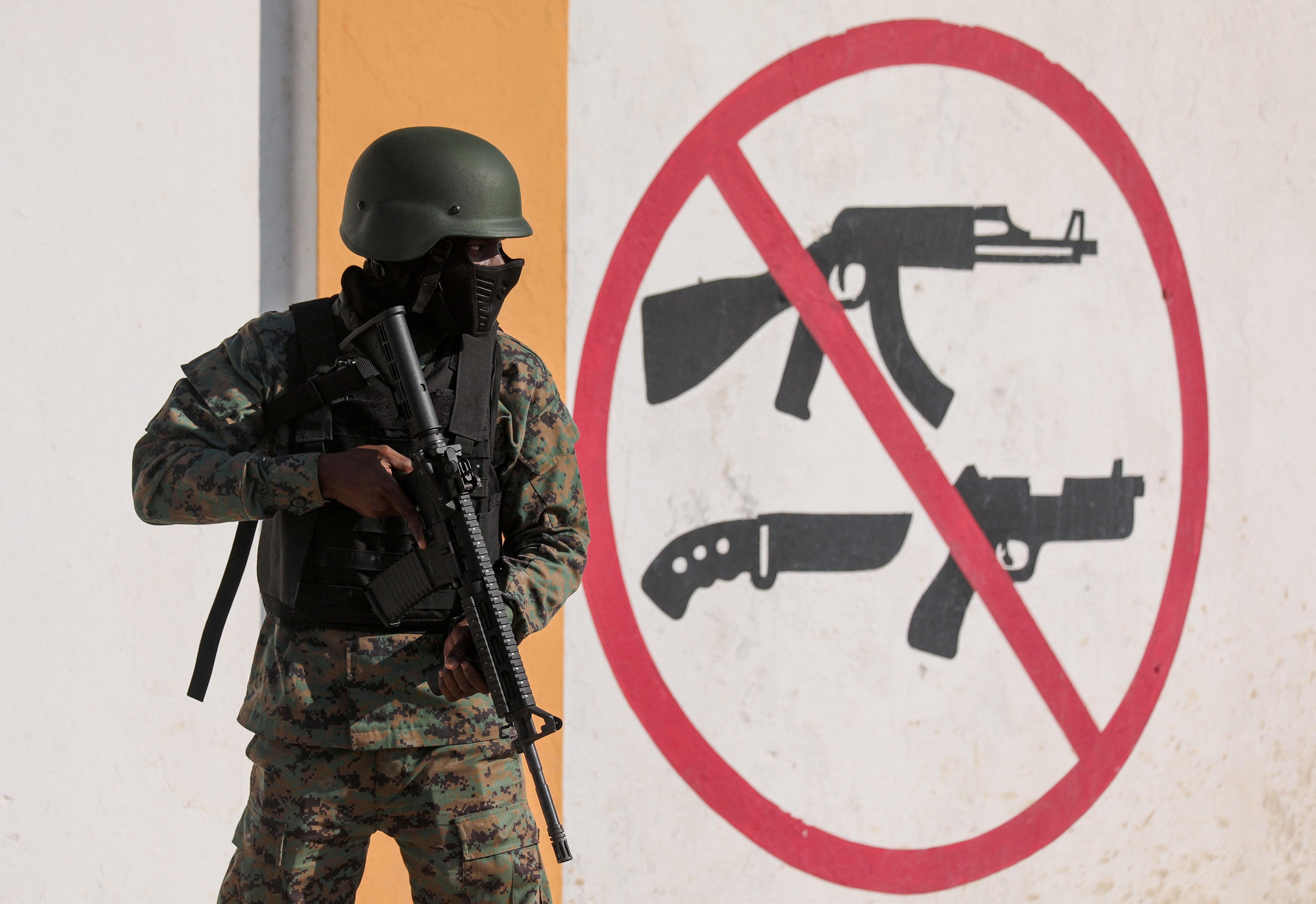 A soldier stands next to a mural prohibiting the use of firearms