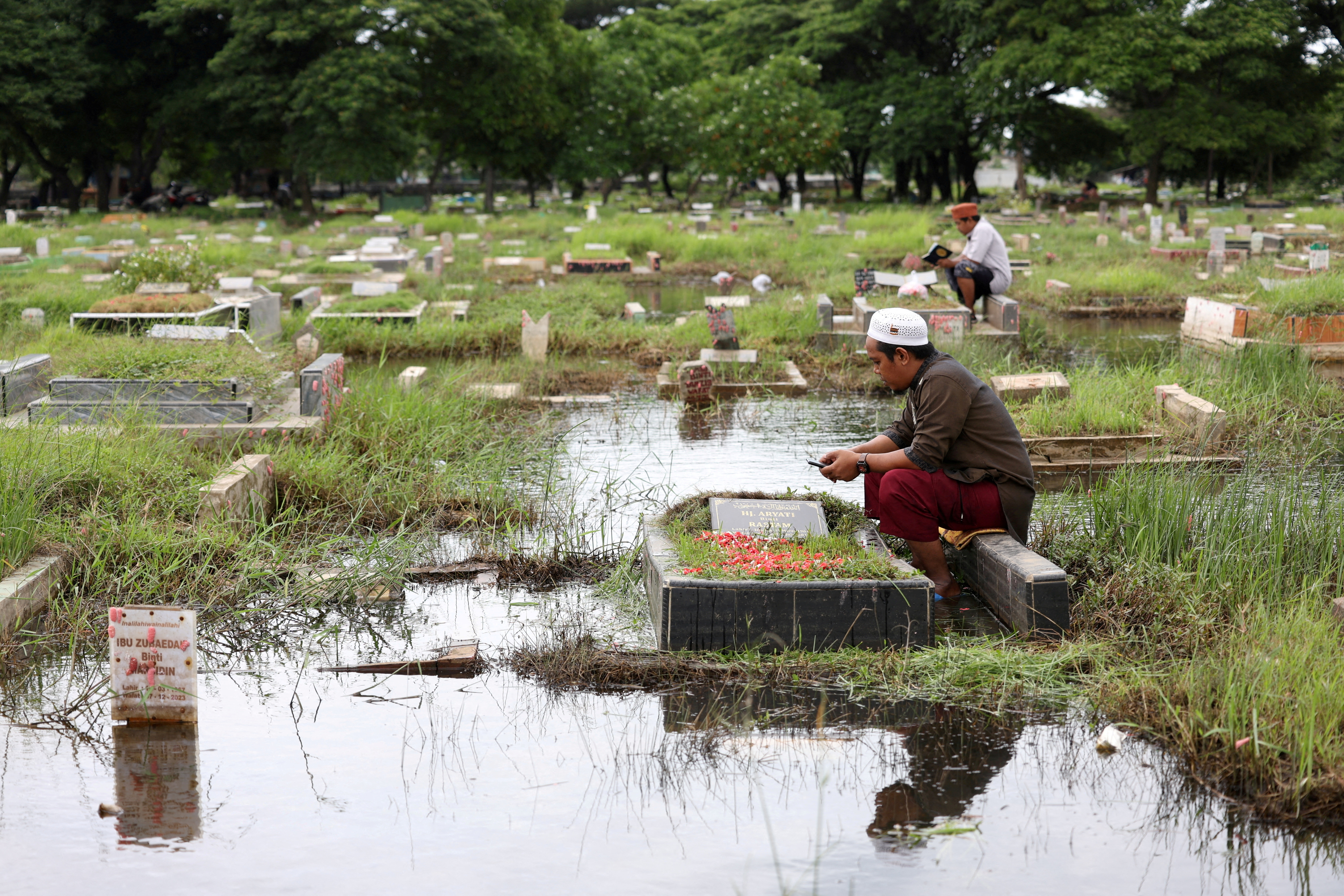 Men pray while visiting their relative's graves submerged in water due to heavy rain ahead of the holy fasting month of Ramadan, at the Semper cemetery complex in North Jakarta, Indonesia, March 8