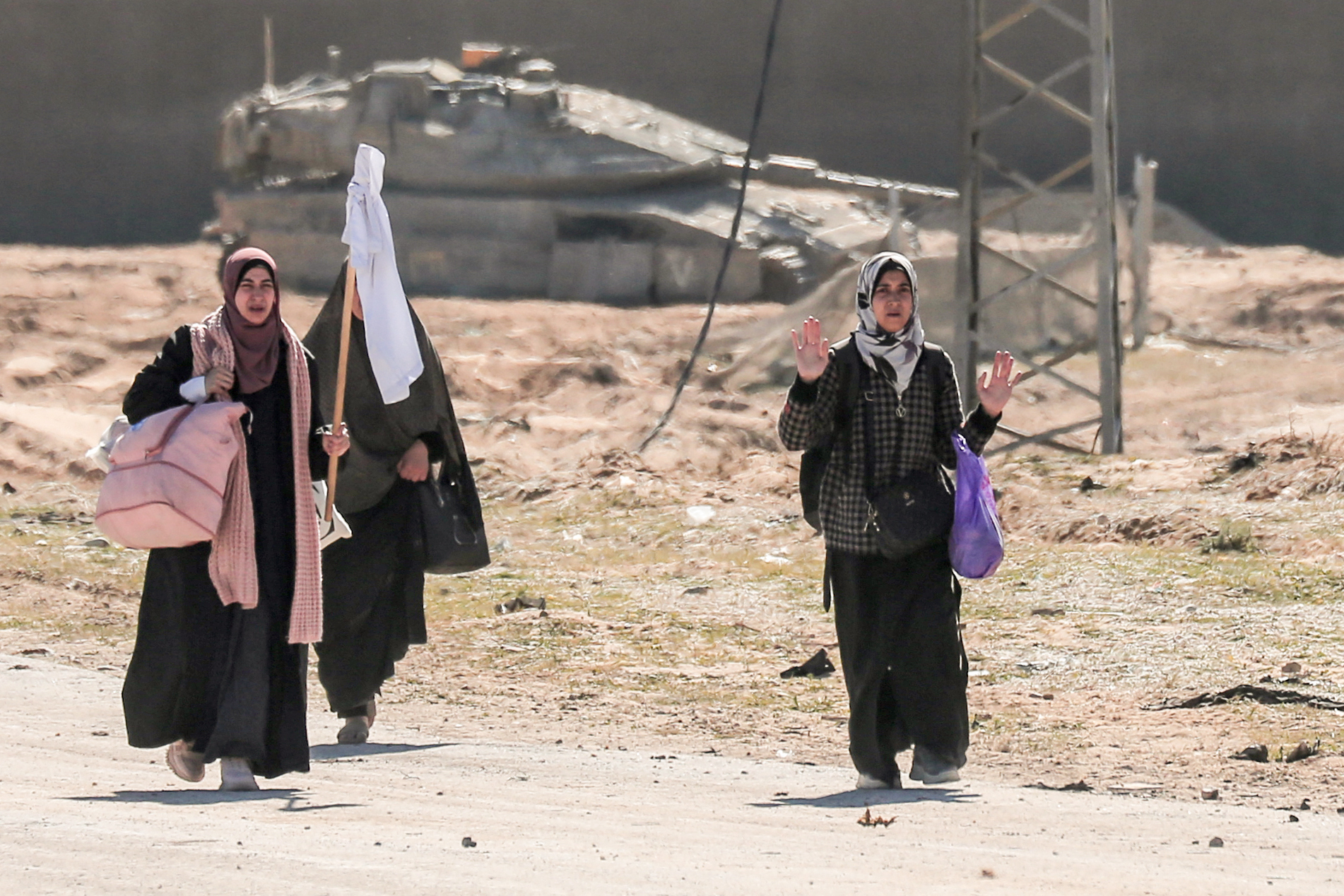 Displaced Palestinian women carrying their belongings lift a makeshift white flag as they walk past Israeli forces while fleeing the Hamad City area in Khan Yunis in the southern Gaza Strip on March 5