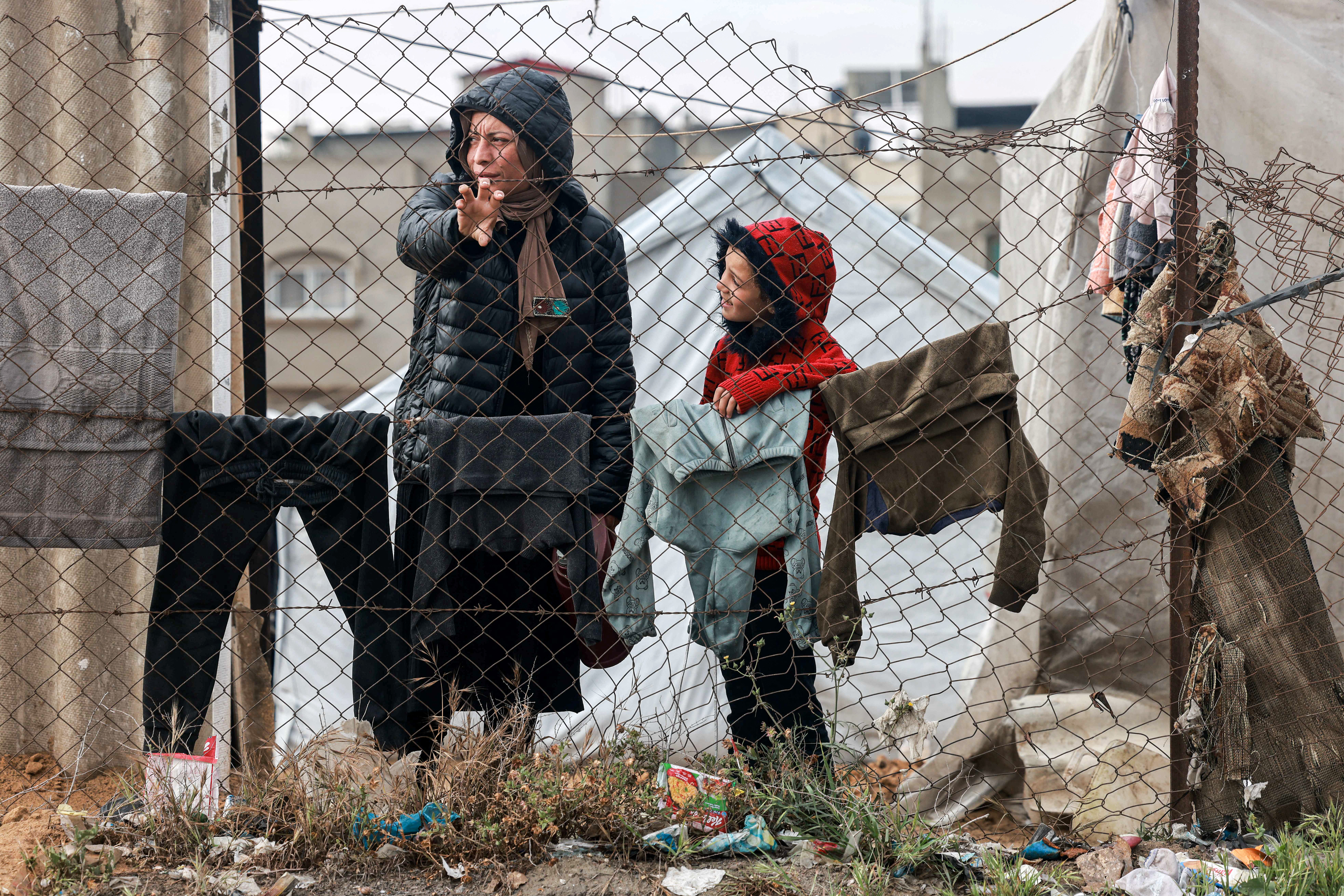 A woman and child stand by drying clothes hanging on a laundry line outside tents housing displaced Palestinians in Rafah in the southern Gaza Strip