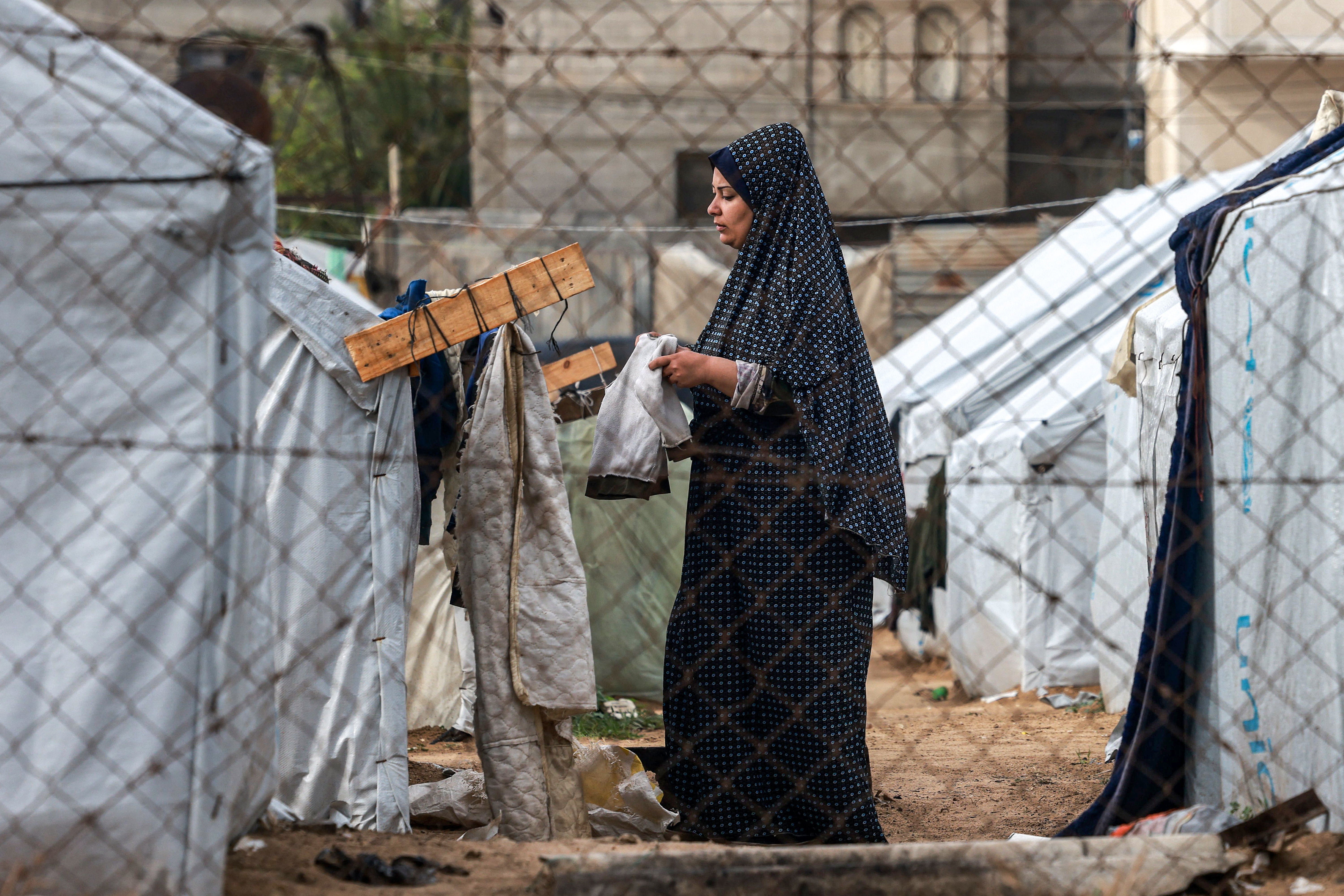 A woman hangs clothes out to dry on a laundry line outside tents housing displaced Palestinians in Rafah in the southern Gaza Strip