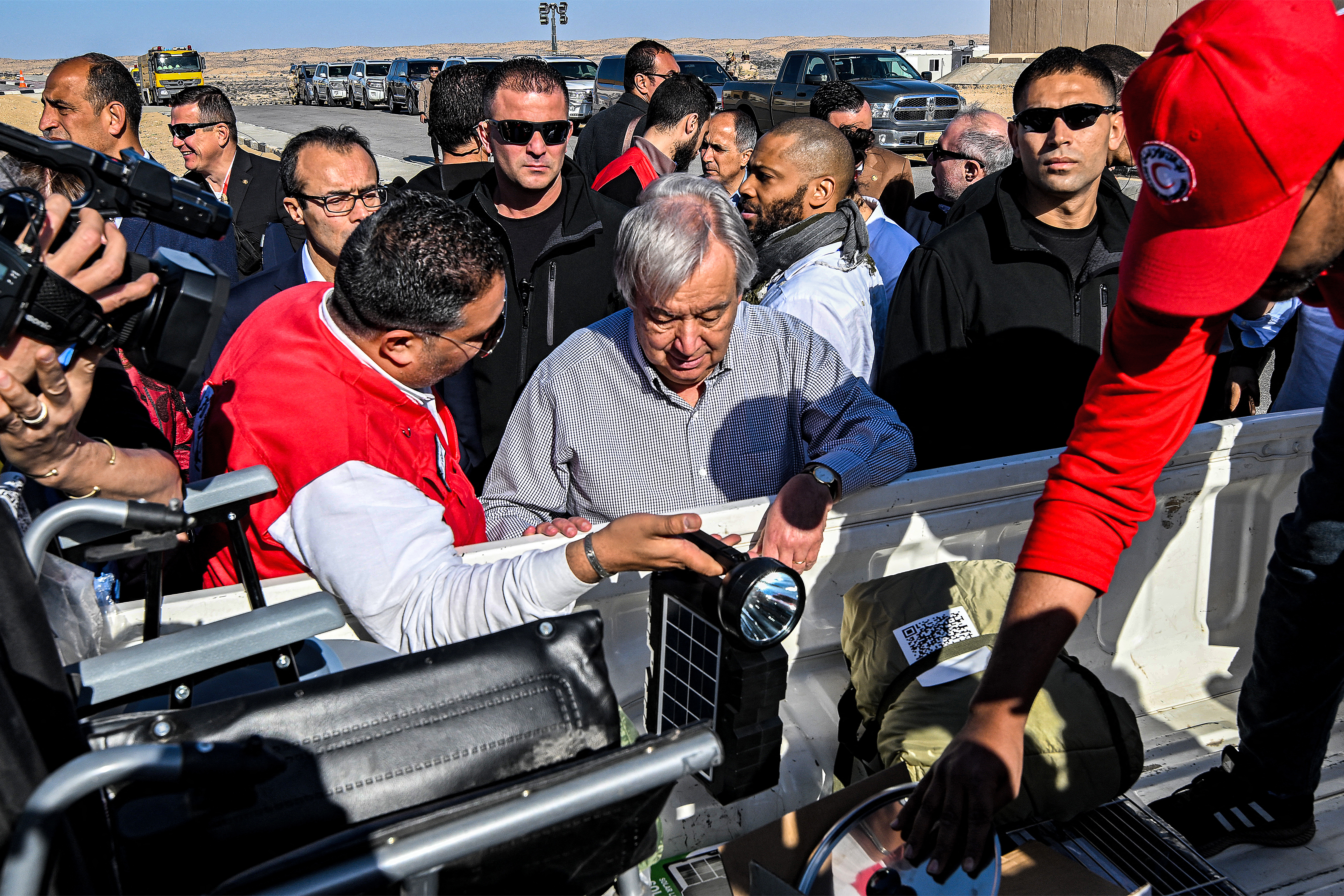 a man in a red vest shows a man wearing grey items including a wheelchair in the back of a truck