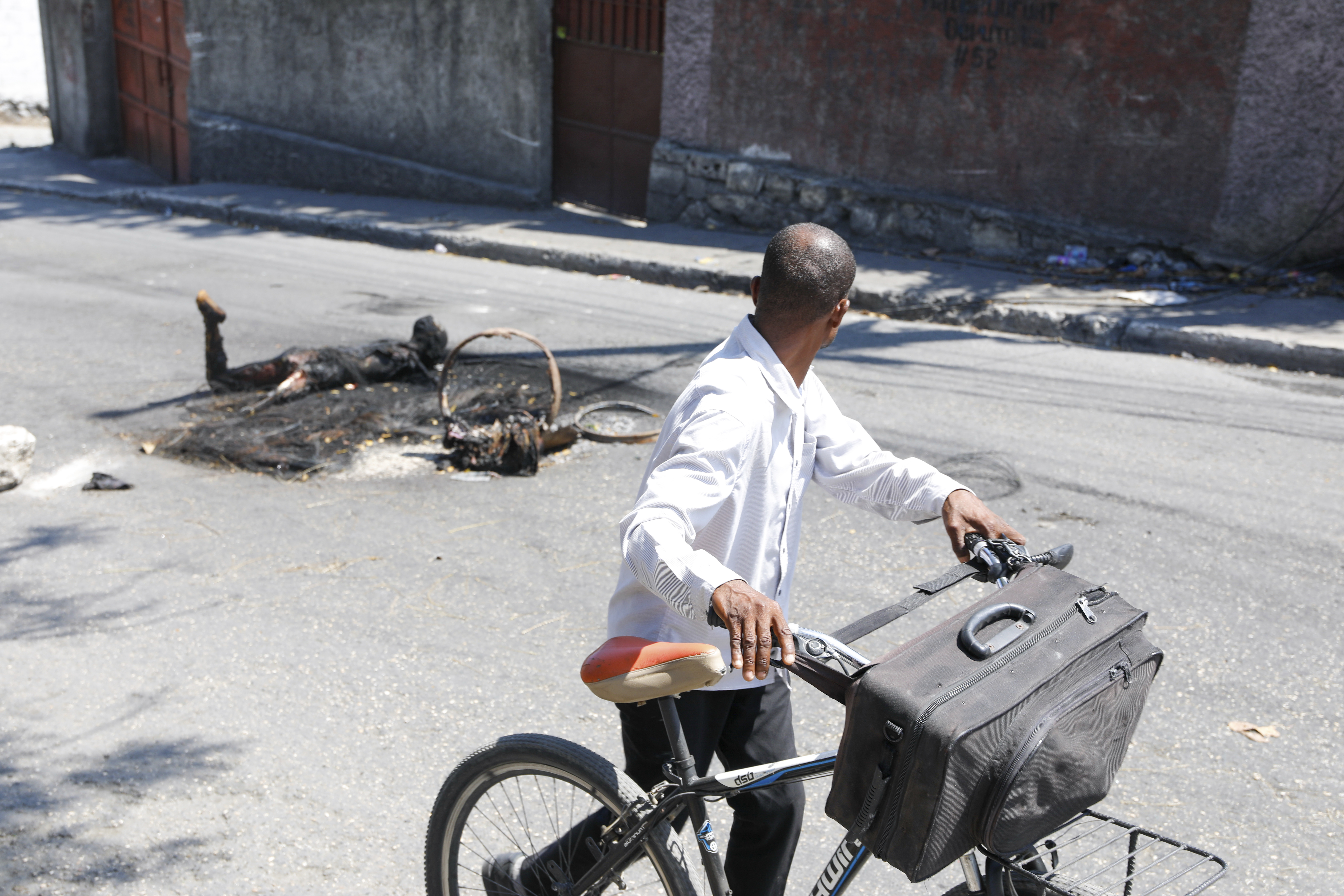 A man pushes his bike past the body of a person who was killed and set on fire in Port-au-Prince,