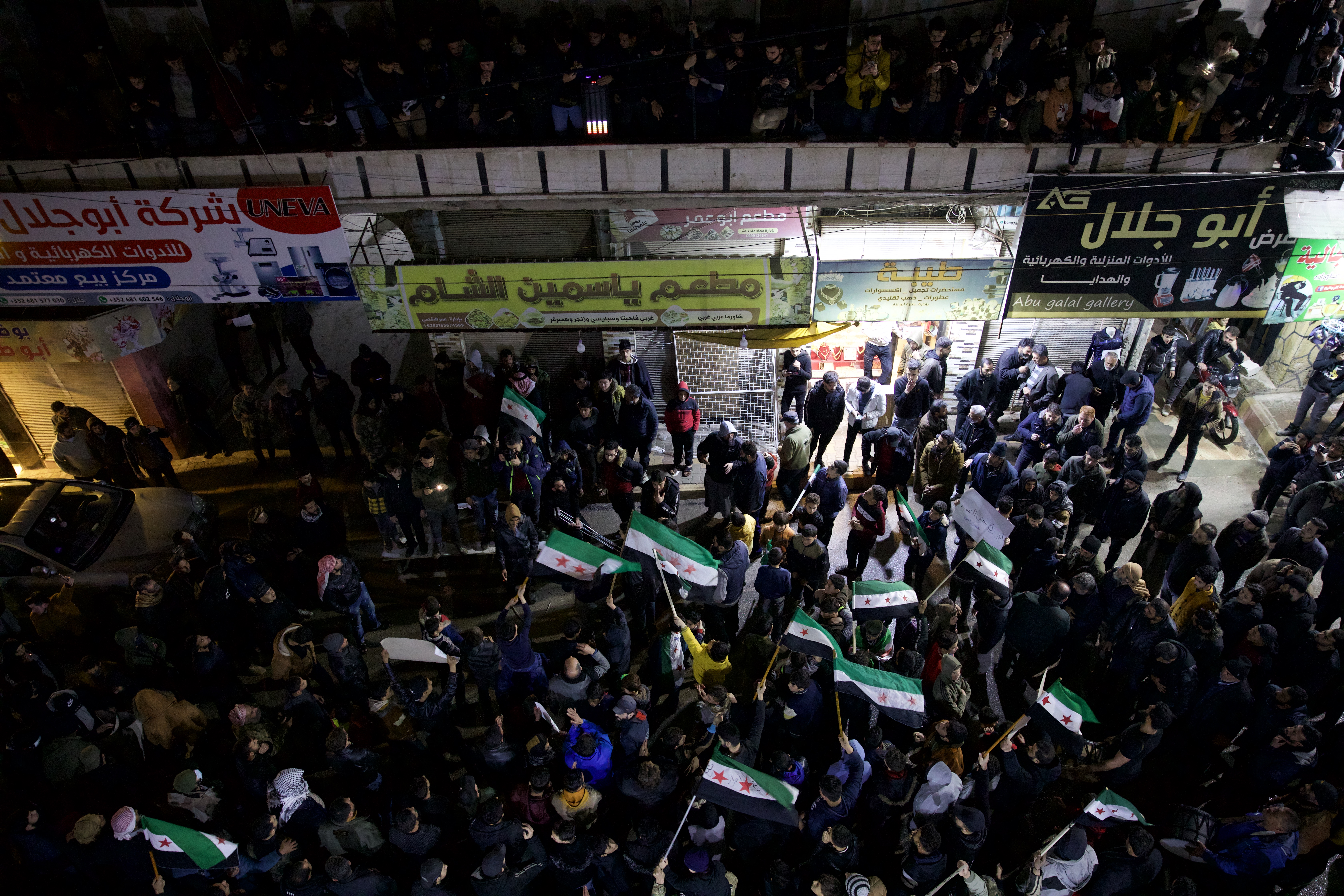 A crowd of protesters, some flying the Syrian opposition flag, gather for a protest. The picture is taken from above.