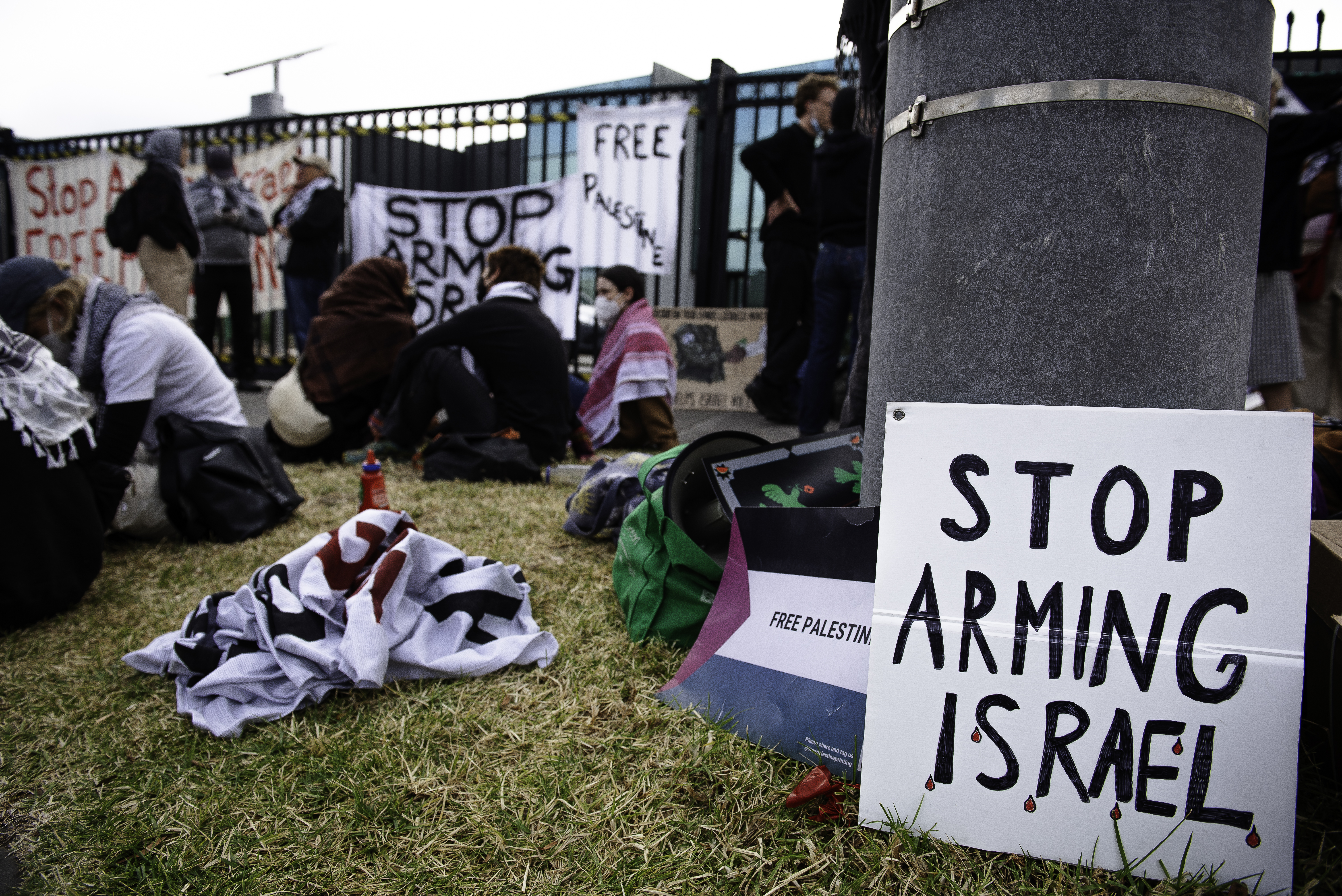 Protesters sitting outside the HTA factory in the Melbourne suburbs,. There is a large placard reading 'Stop arming Israel"