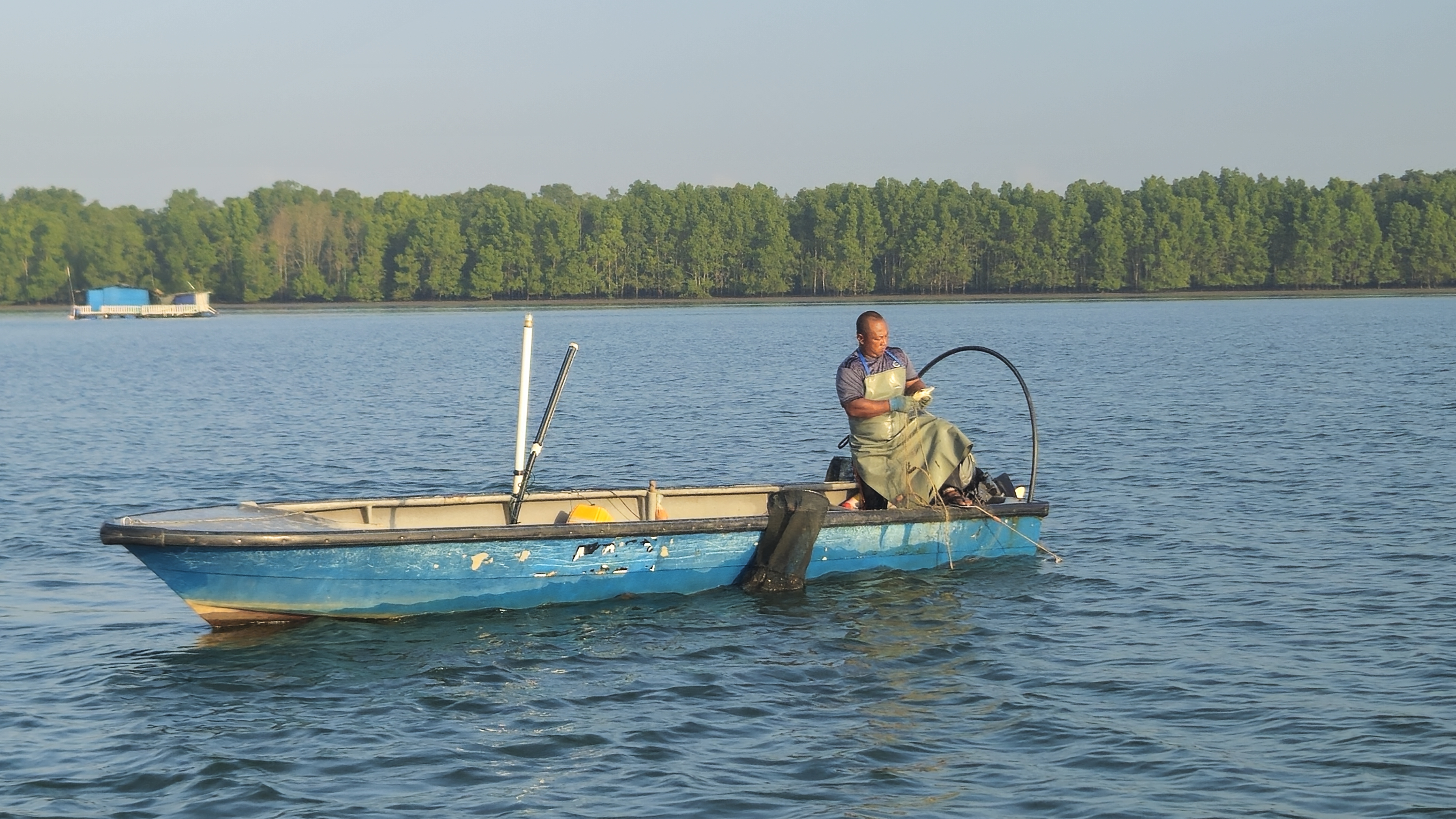 Faizan Wahid on his boat off Johor. He is wearing waders. The boat has blue hull. Mangroves can be seen behind him. 