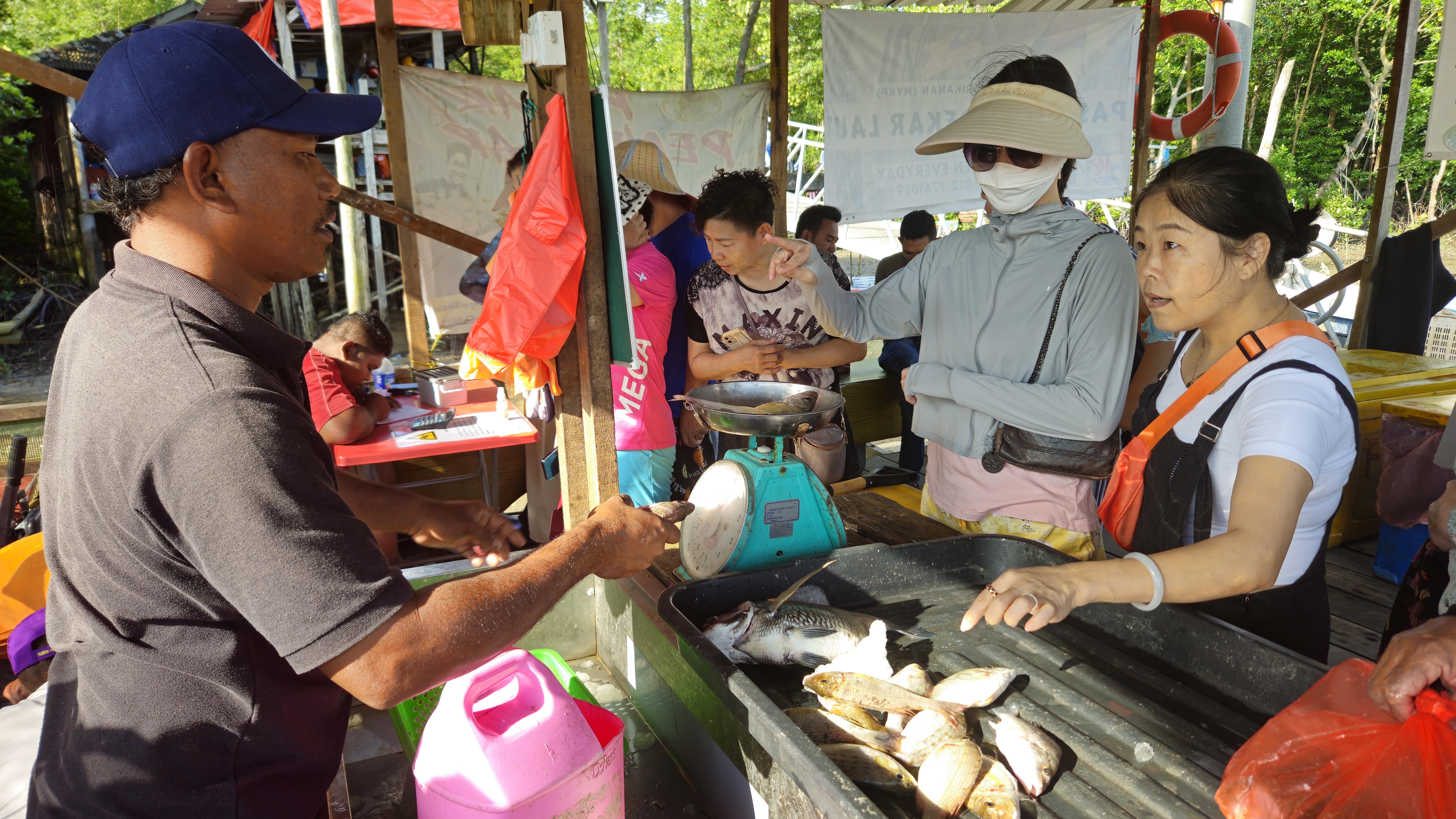 A fish market at a jetty near Pendas. A trader is speaking to a customer about what's available.