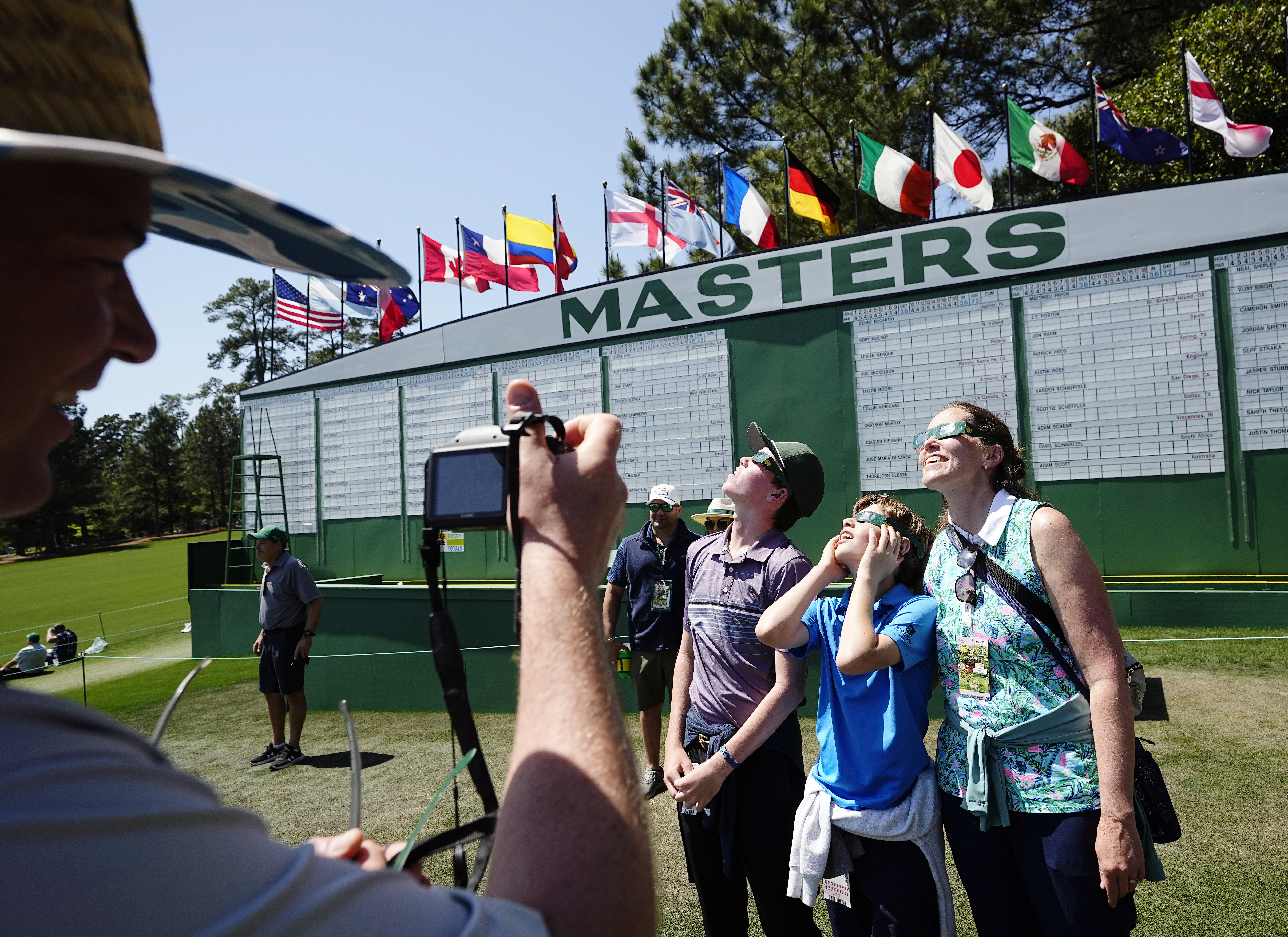 A man takes a photo of three people wearing eclipse glasses.