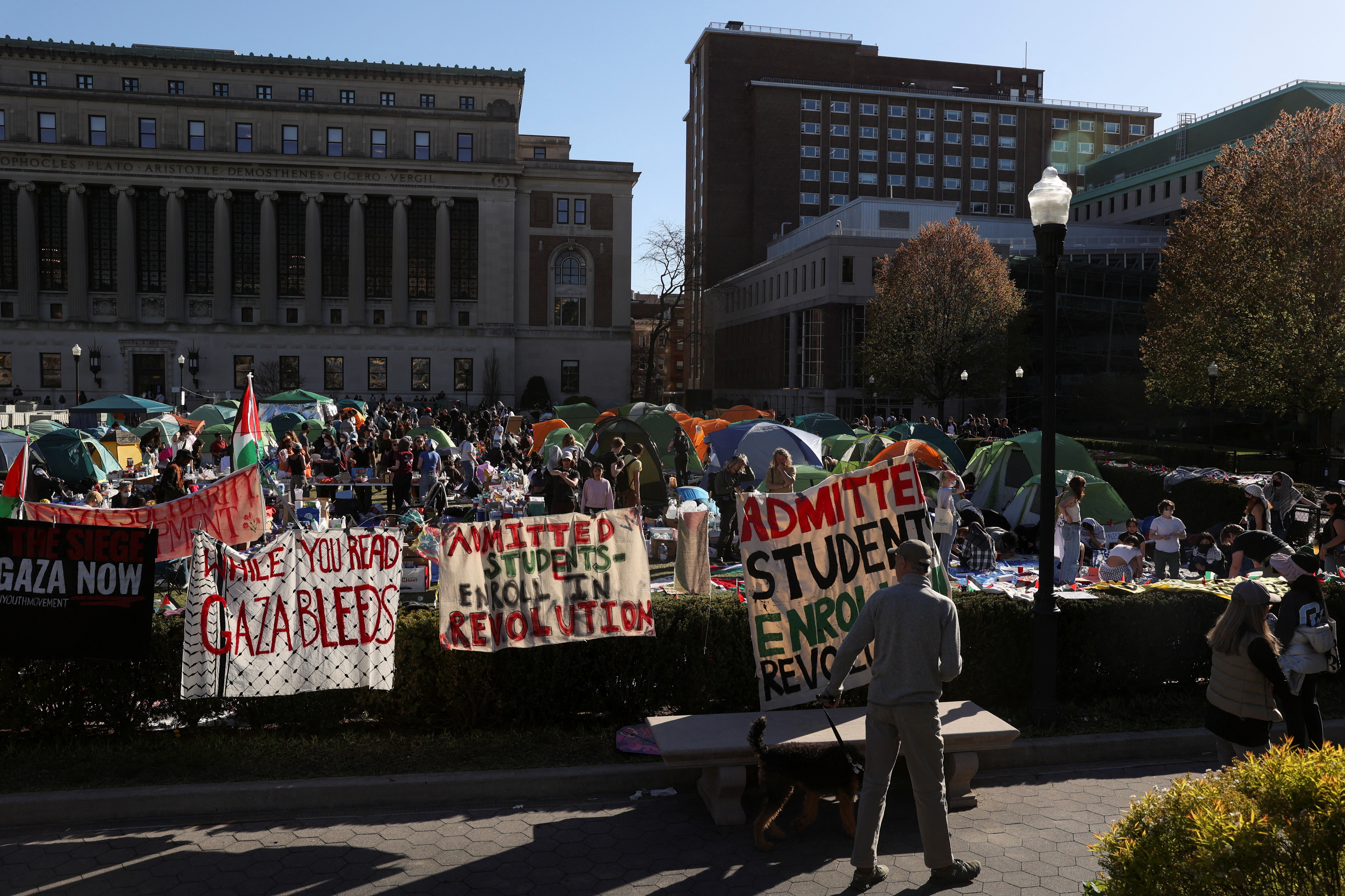 A man walking his dog stops to look at the area where students continue to hold a protest in support of Palestinians at Columbia University, in New York City, U.S.
