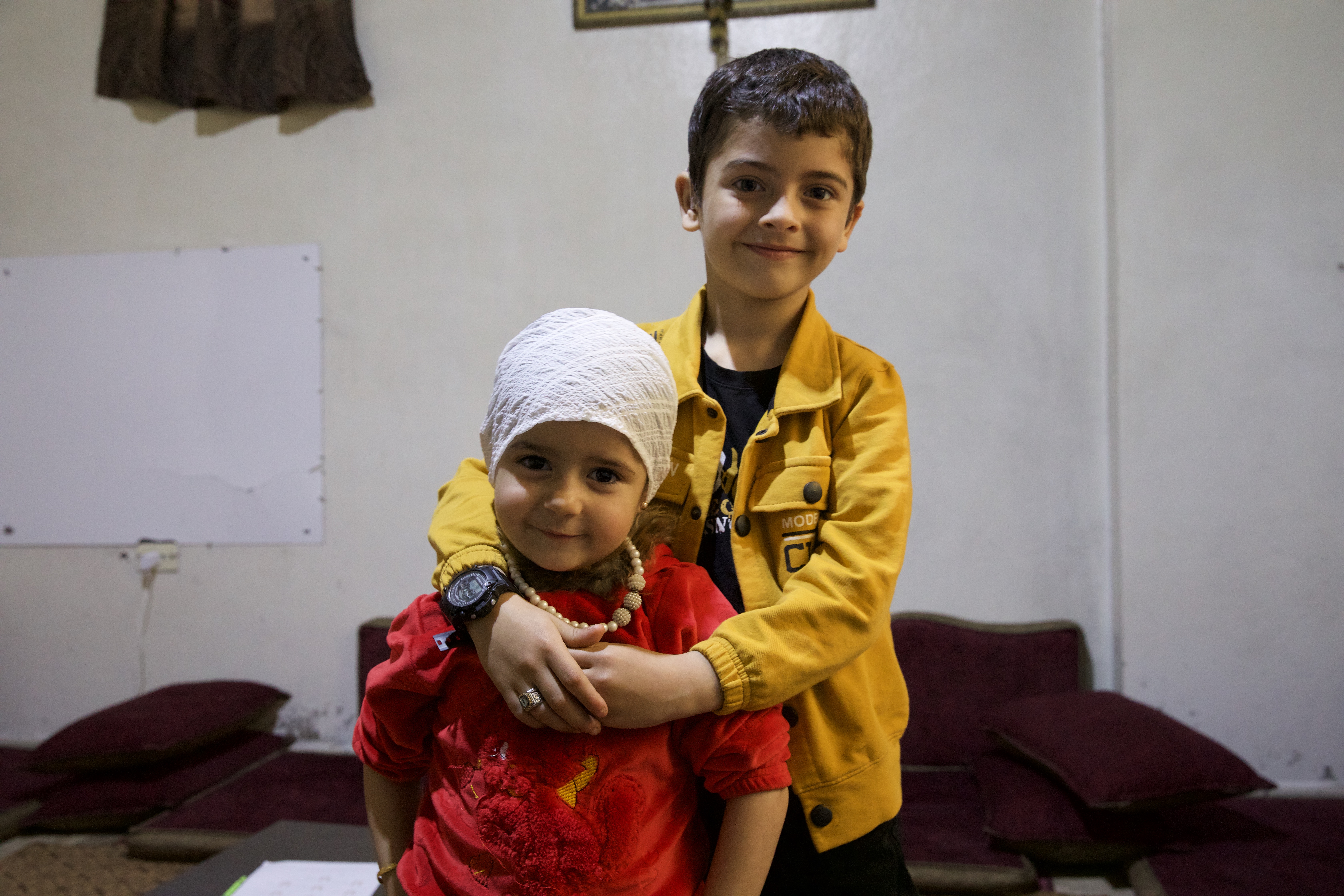 Aslan and Celine in their living room, dressed snazzily and smiling large in their home in Idlib, Syria