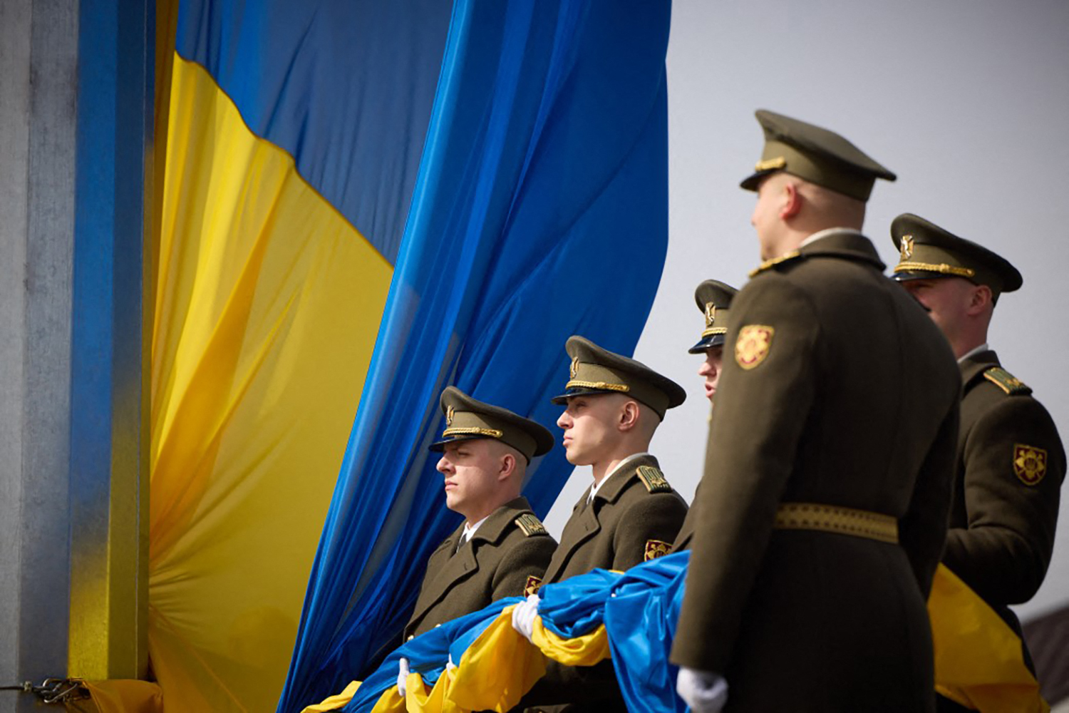 Ukrainian servicemen raising the flag of Ukraine at a memorial to the victims of the Russian occupation in the town of Bucha, There are Ukrainian flags behind them,