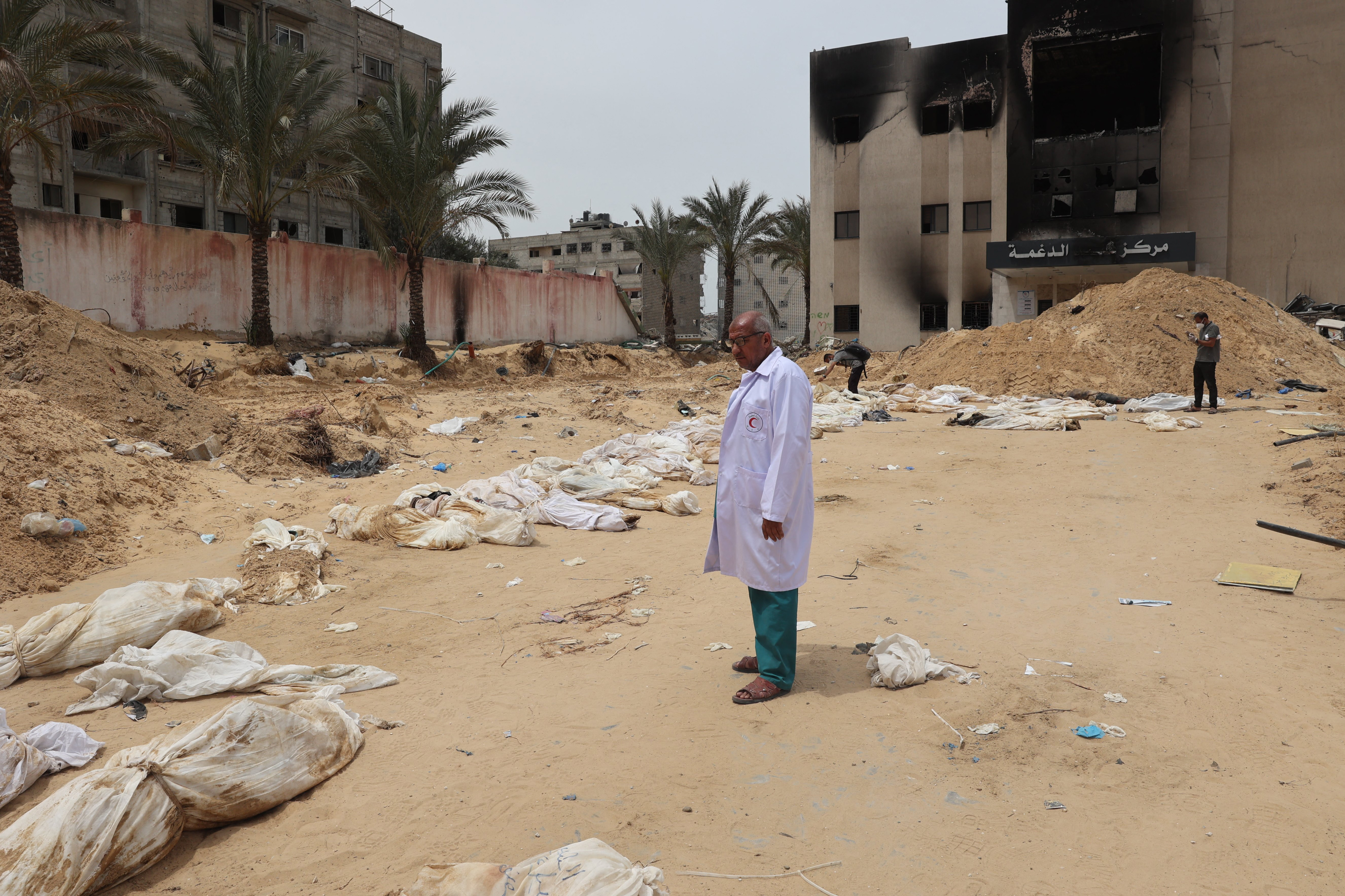 A doctor stands near bodies lined up for identification after they were unearthed from a mass grave found in the Nasser Medical Complex in the southern Gaza Strip on April 25, 2024.edical Complex.