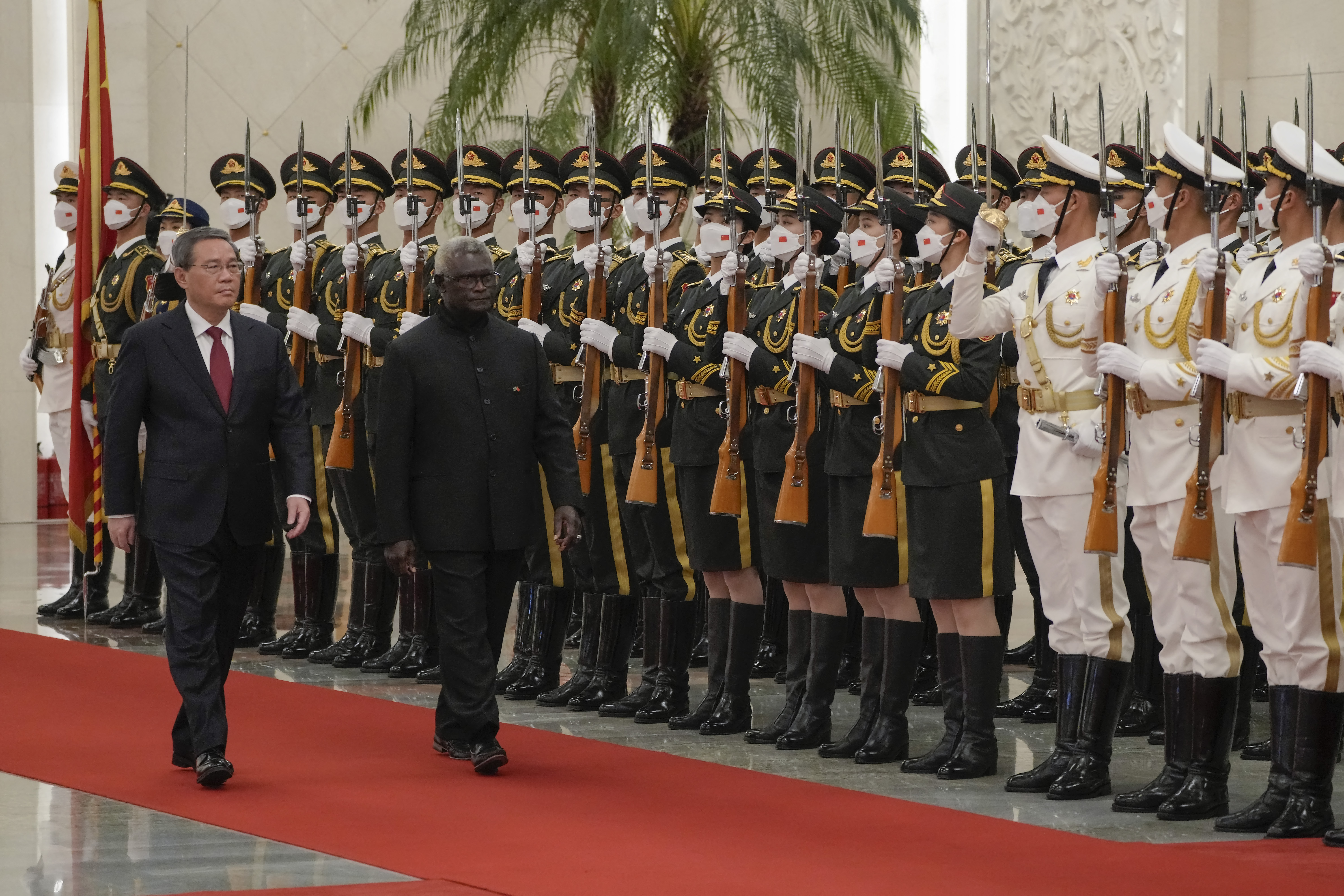 Manasseh Sogavare and China's Premier Li Qiang walking past an honour guard in Beijing. The giards are on the right. The two men are walking on a red carpet and Sogavare is nearest the guards.