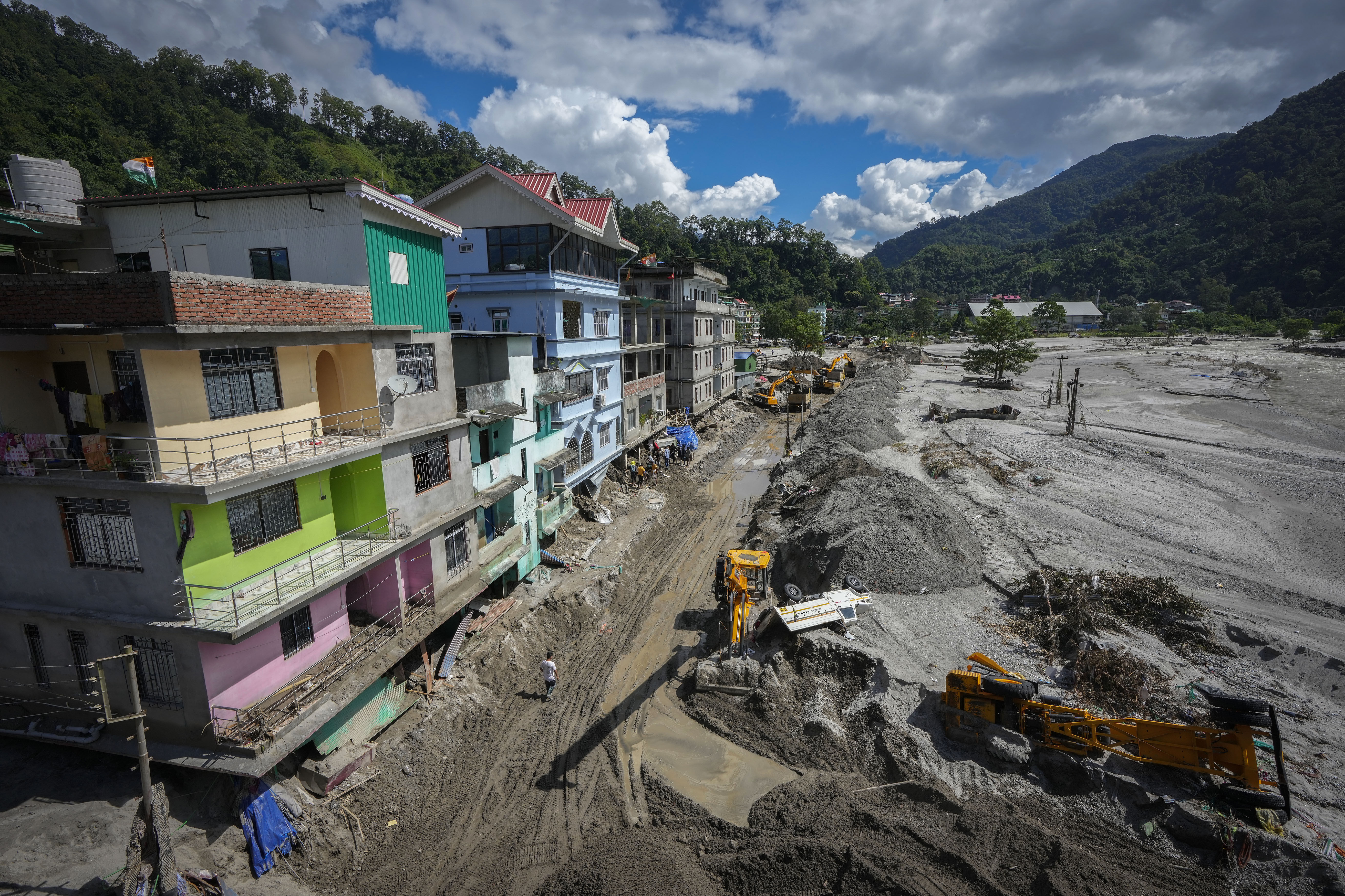 Vehicles that got washed away in floods lie on the sand as machinery is used to clean mud and sand near the buildings along the Teesta river in Rongpo, east Sikkim, India