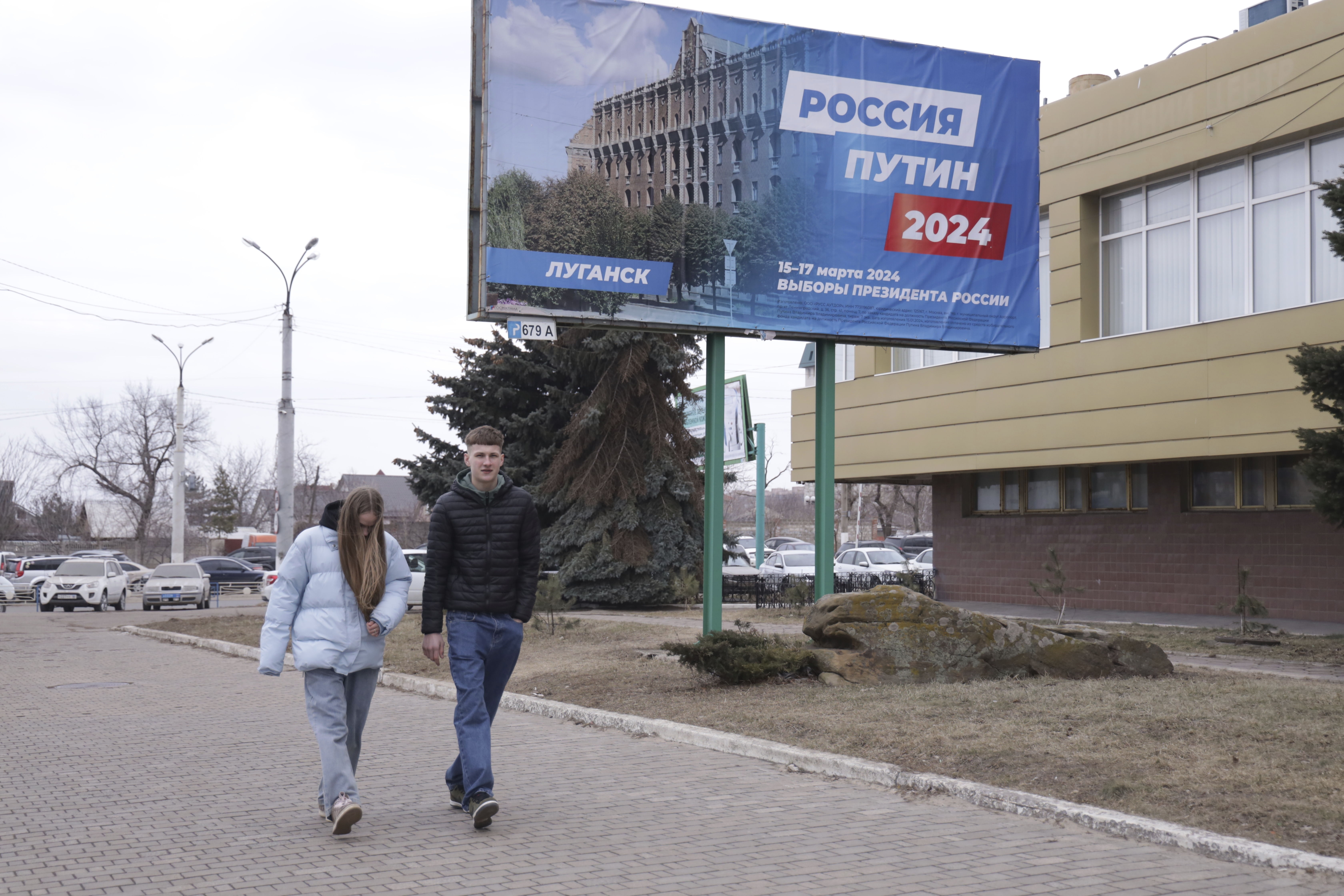 A couple walk past a billboard which promotes the upcoming presidential election with words in "Russian: Russia, Putin, 2024" in a street in Luhansk, the capital of Russian-controlled Luhansk region, eastern Ukraine, on Thursday, March 14, 2024. Russian President Vladimir Putin Thursday called on people in Ukraine's occupied regions to vote, telling them and Russians that participation in the elections is "manifestation of patriotic feeling," Presidential elections are scheduled in Russia for March 17. (AP Photo)